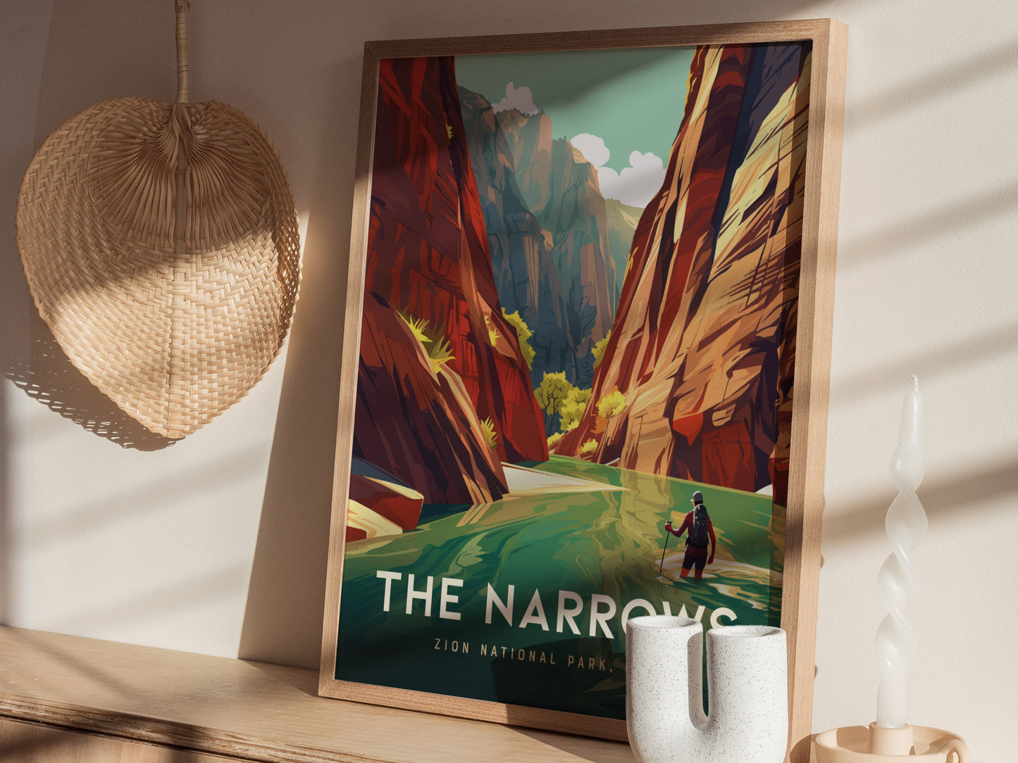 A framed poster of The Narrows at Zion National Park with vibrant canyon walls and a hiker in the river, displayed on a wooden shelf beside a wicker basket and.