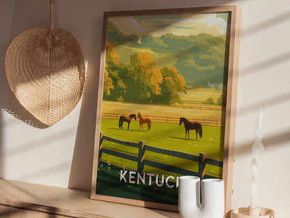 A framed poster depicting a Kentucky landscape with horses grazing in a green pasture, set against a wooden table with a woven hat and decorative candle nearby.
