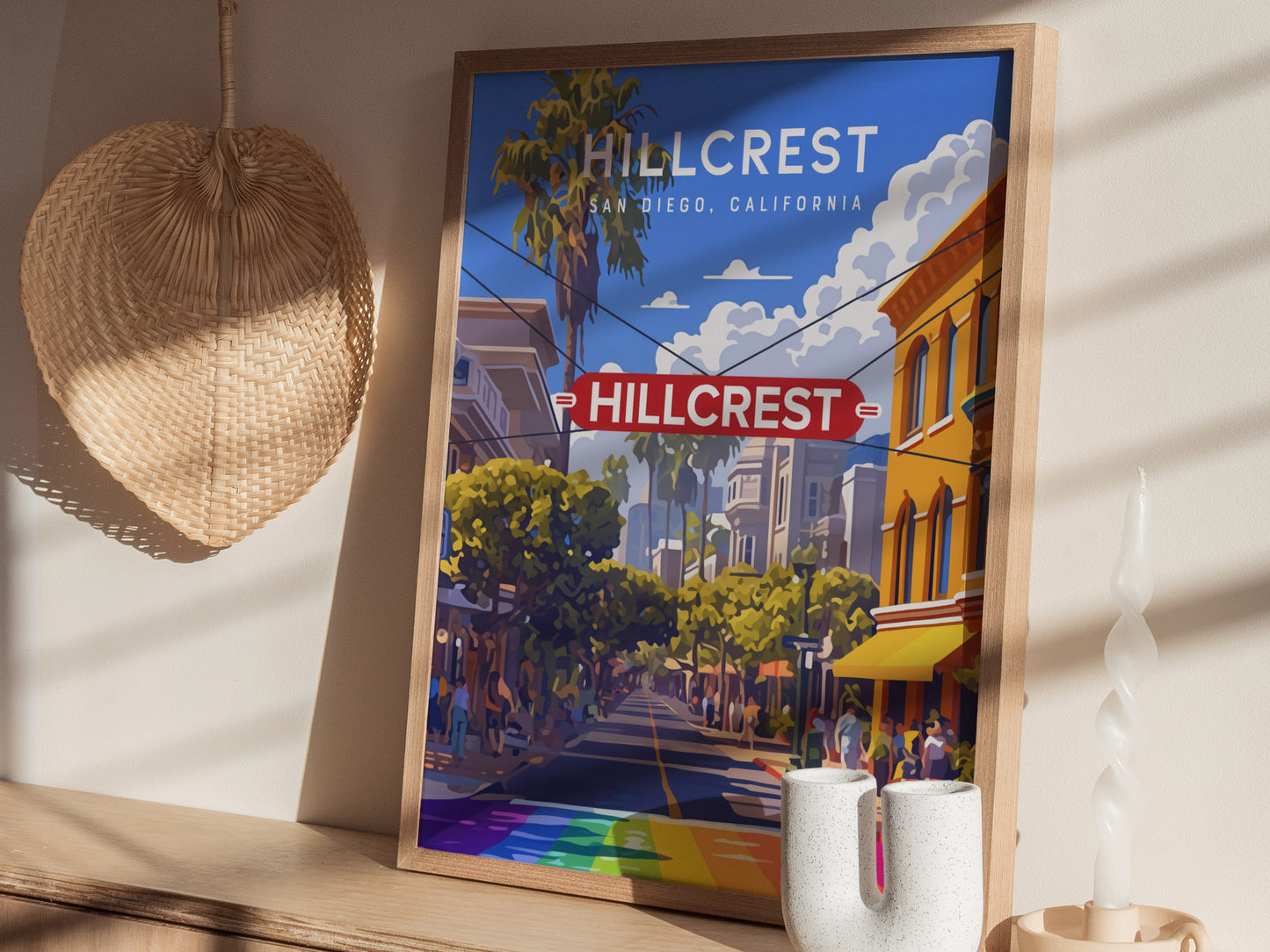 Framed Hillcrest poster featuring the iconic sign and a vibrant street scene with a rainbow crosswalk. Its displayed on a wooden shelf with a woven basket and decorative candle.