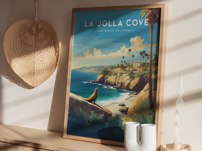 A framed La Jolla Cove poster depicting a scenic coastal view with cliffs, palm trees, and a sea lion. It rests on a shelf near a woven basket and abstract.