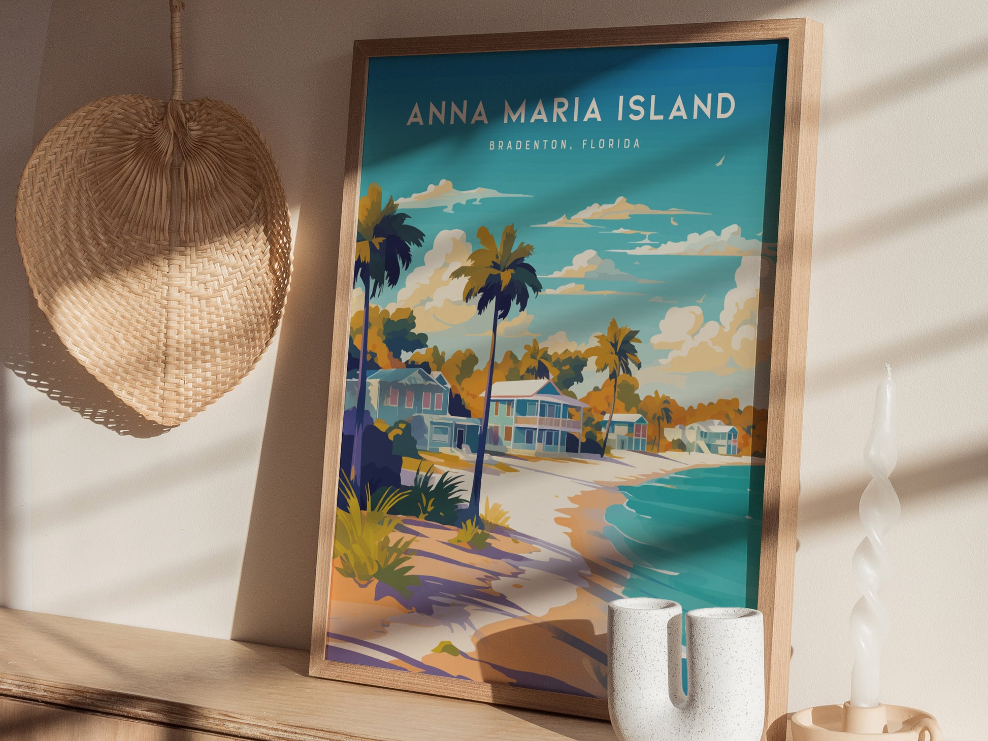 A framed poster of Anna Maria Island, Bradenton, Florida, features vibrant beach cottages, palm trees, and a serene shoreline under a blue sky. The scene is complemented by a wicker basket and a twisted candle on a wooden surface.