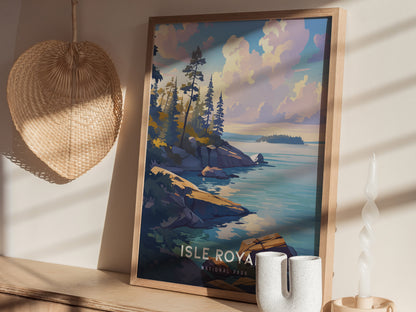A framed Isle Royale National Park poster on a wooden surface, depicting a scenic shoreline with trees and clouds. A woven basket and a sculpted candle are nearby.