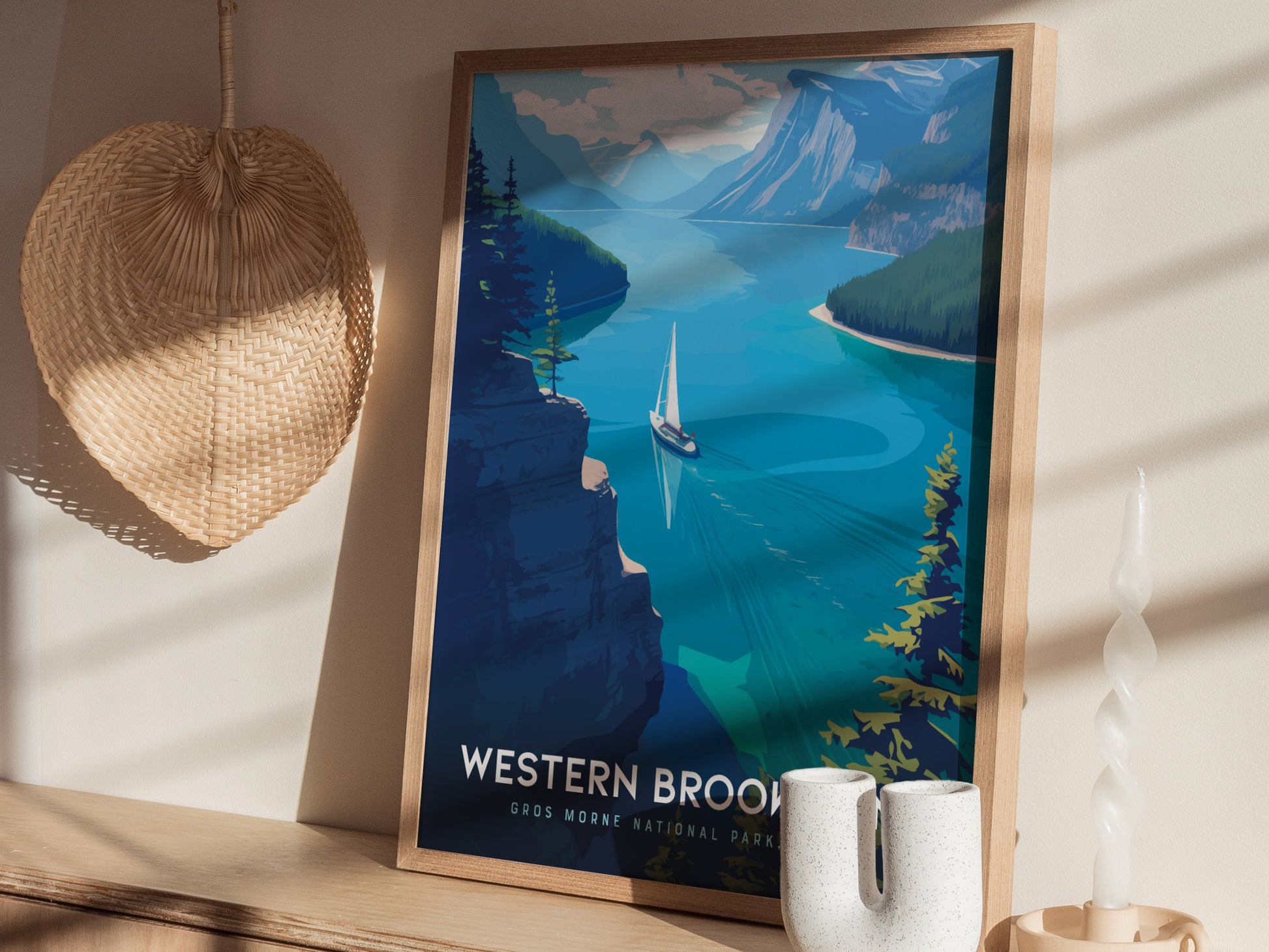 A framed poster of Western Brook Pond featuring a sailboat on blue waters with towering cliffs is displayed on a wooden shelf beside a wicker basket and decorative candle.