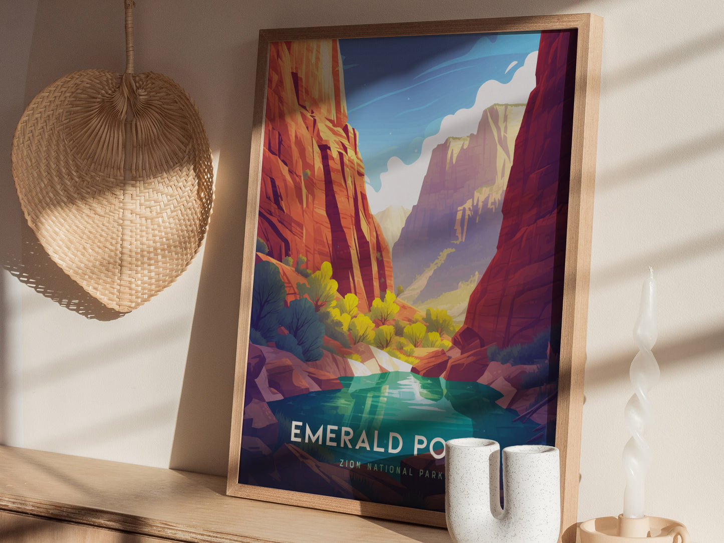 A framed poster of Zion National Parks Emerald Pools is displayed on a wooden shelf, accompanied by a woven wall decor, ceramic vases, and a twisted candle.