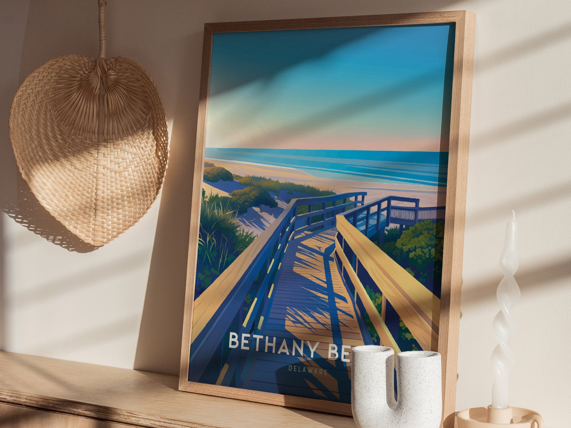 A framed poster of Bethany Beach, Delaware with a wooden boardwalk leading to the ocean is displayed on a shelf beside a woven wall hanging and decorative candle.