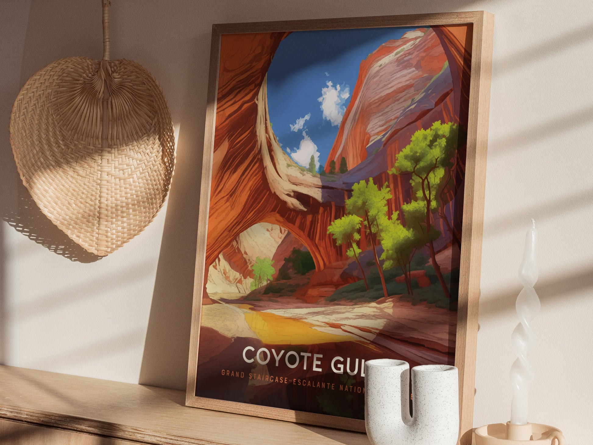 A framed poster of Coyote Gulch with vibrant canyon walls and trees is displayed on a wooden surface, alongside a woven wall decor and a twisted candle.
