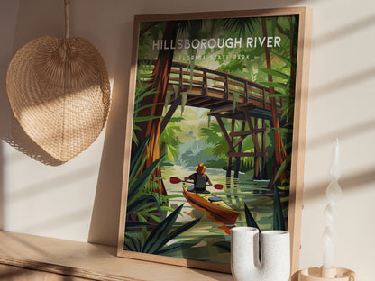 A framed poster of Hillsborough River State Park depicts a kayaker beneath a wooden bridge, surrounded by lush greenery.