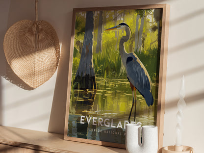 A framed poster of a Great Blue Heron standing in water, surrounded by lush greenery, is displayed on a wooden shelf next to a wicker basket and a twisted candle.