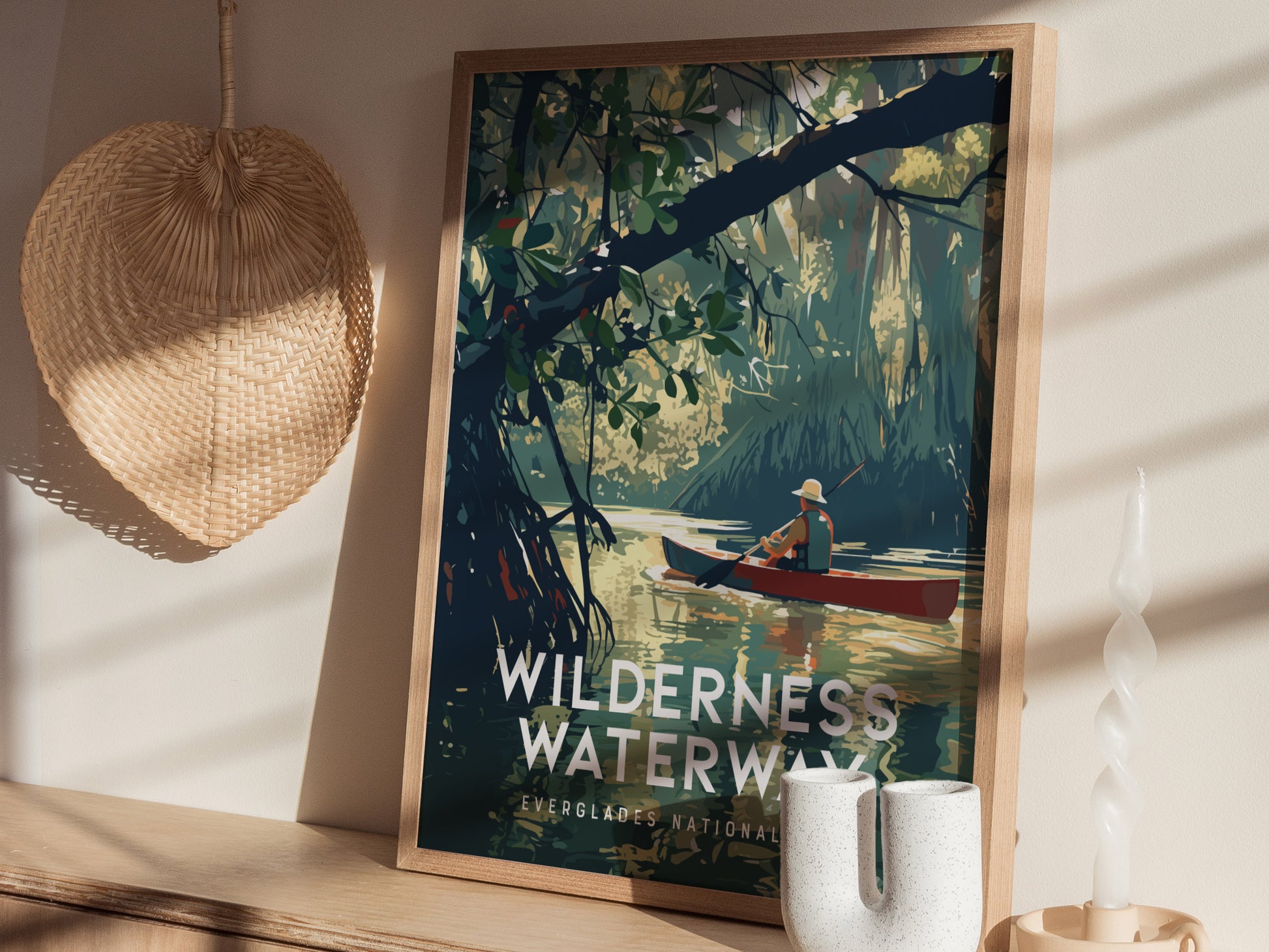 A framed poster of a canoeist navigating calm waters in a lush mangrove forest is displayed on a shelf, accompanied by a woven basket and a twisted candle.