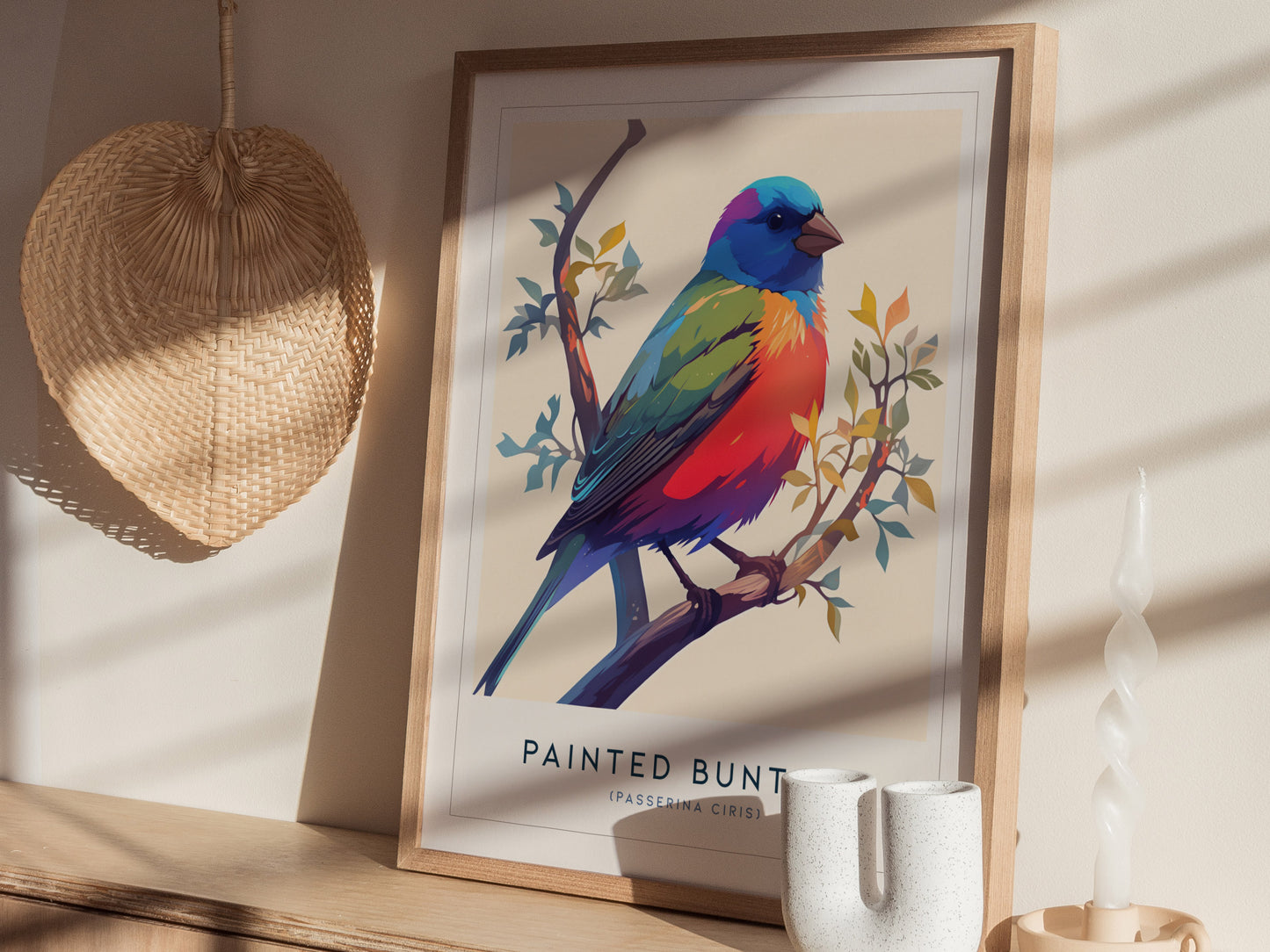 A colorful art print of a painted bunting bird perched on a branch is displayed in a light-filled room. The print features vibrant hues of blue, green, red, and yellow, framed in a natural wood frame.