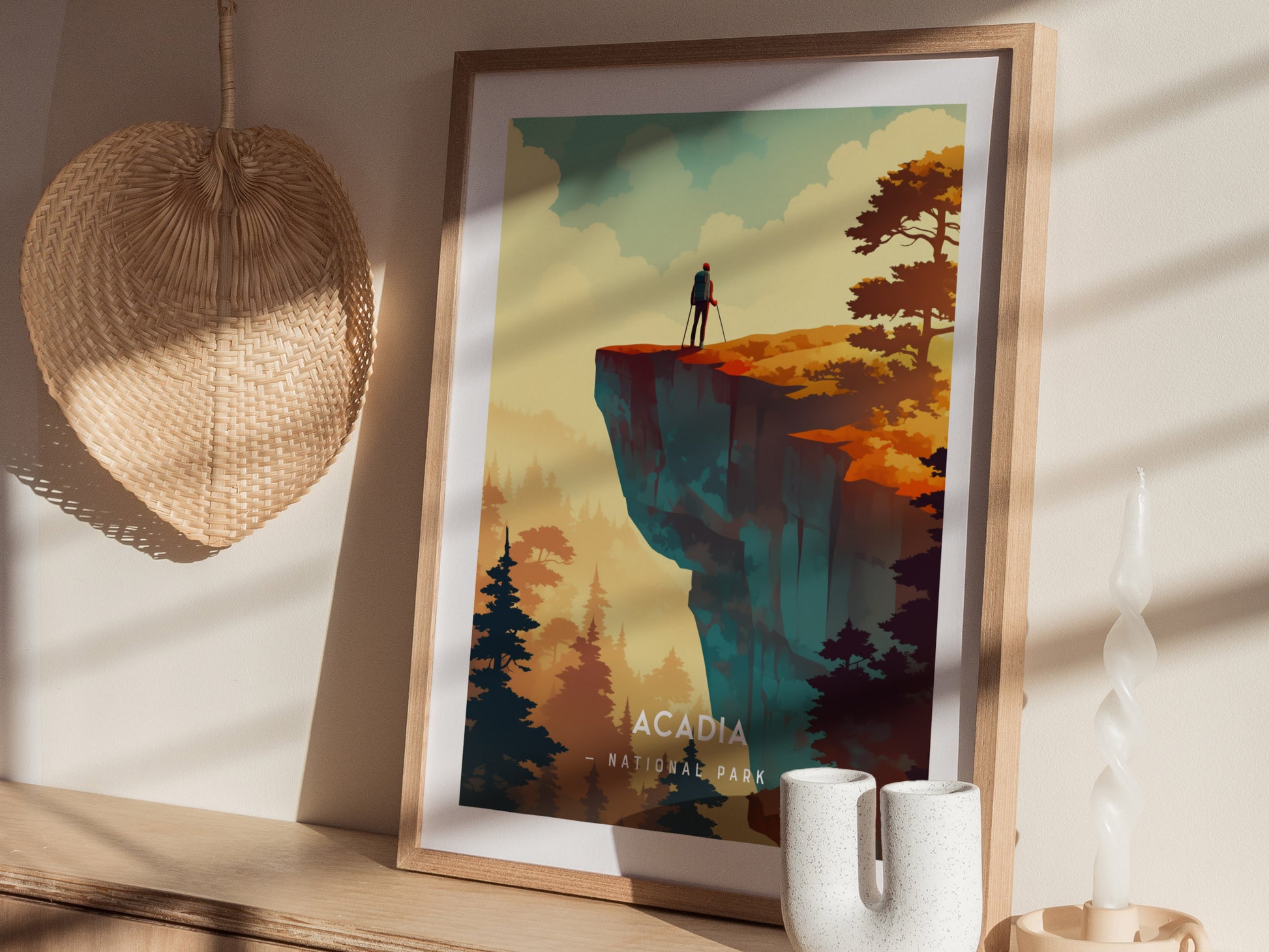 A framed poster of Acadia National Park features a minimalist illustration with a solitary figure on a cliff, surrounded by trees. Its displayed on a wooden shelf with decorative items.
