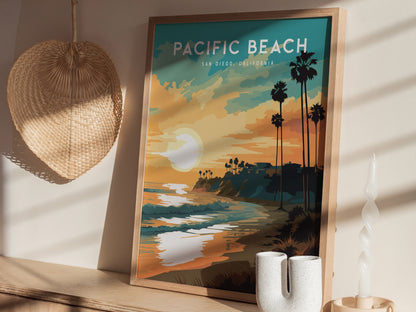 A framed poster of Pacific Beach, San Diego, featuring a colorful sunset over the ocean with palm trees silhouetted against the sky. The poster is set on a shelf beside a woven basket and a decorative candle.