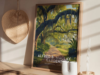 Framed poster of Alfred B. Maclay Gardens with moss-draped trees and a winding path, displayed on a wooden shelf next to a woven fan and decorative candle.