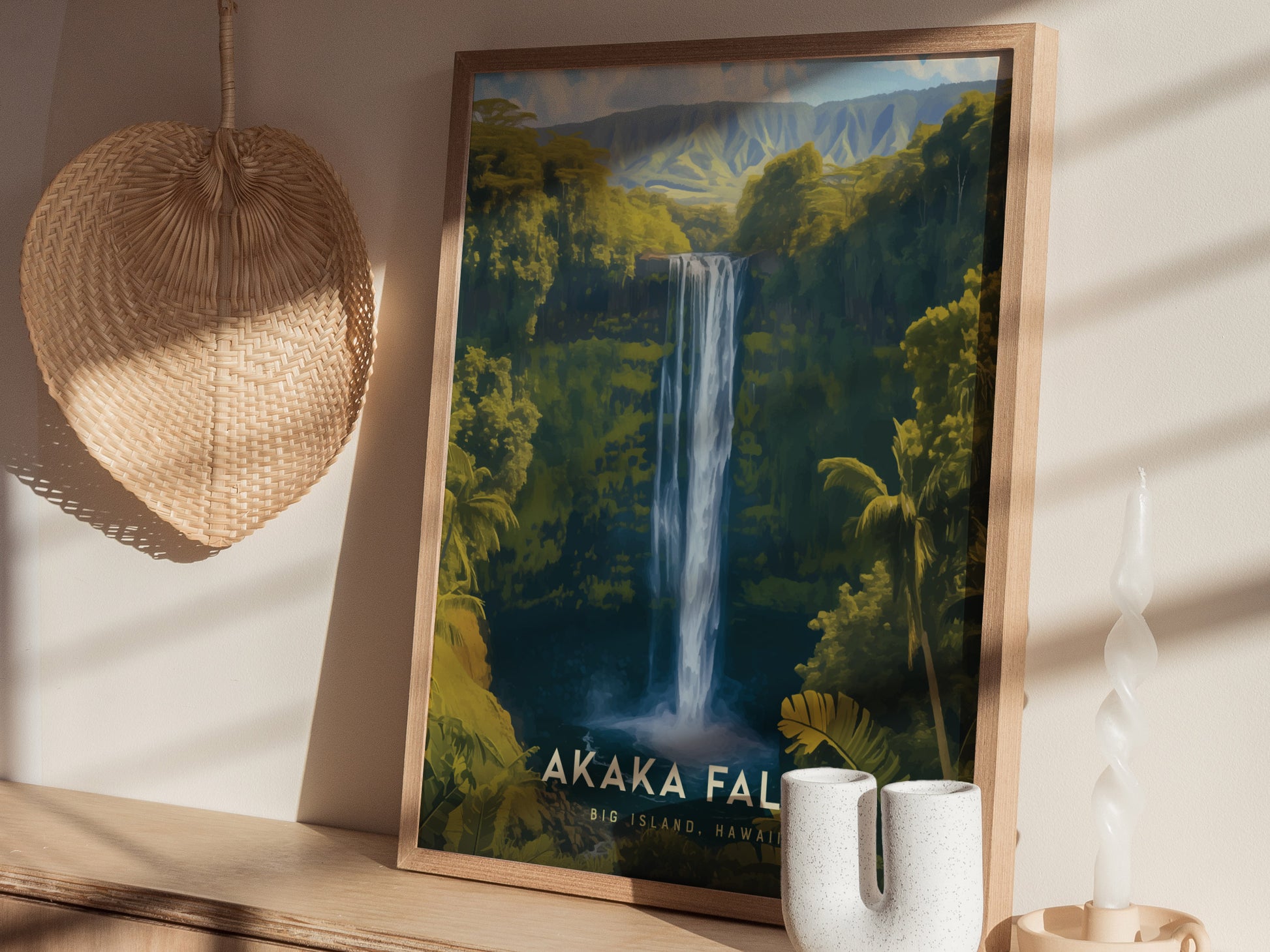 A framed poster depicting Akaka Falls surrounded by lush greenery is displayed on a shelf. Nearby are a woven fan and a twisted white candle, creating a serene atmosphere.