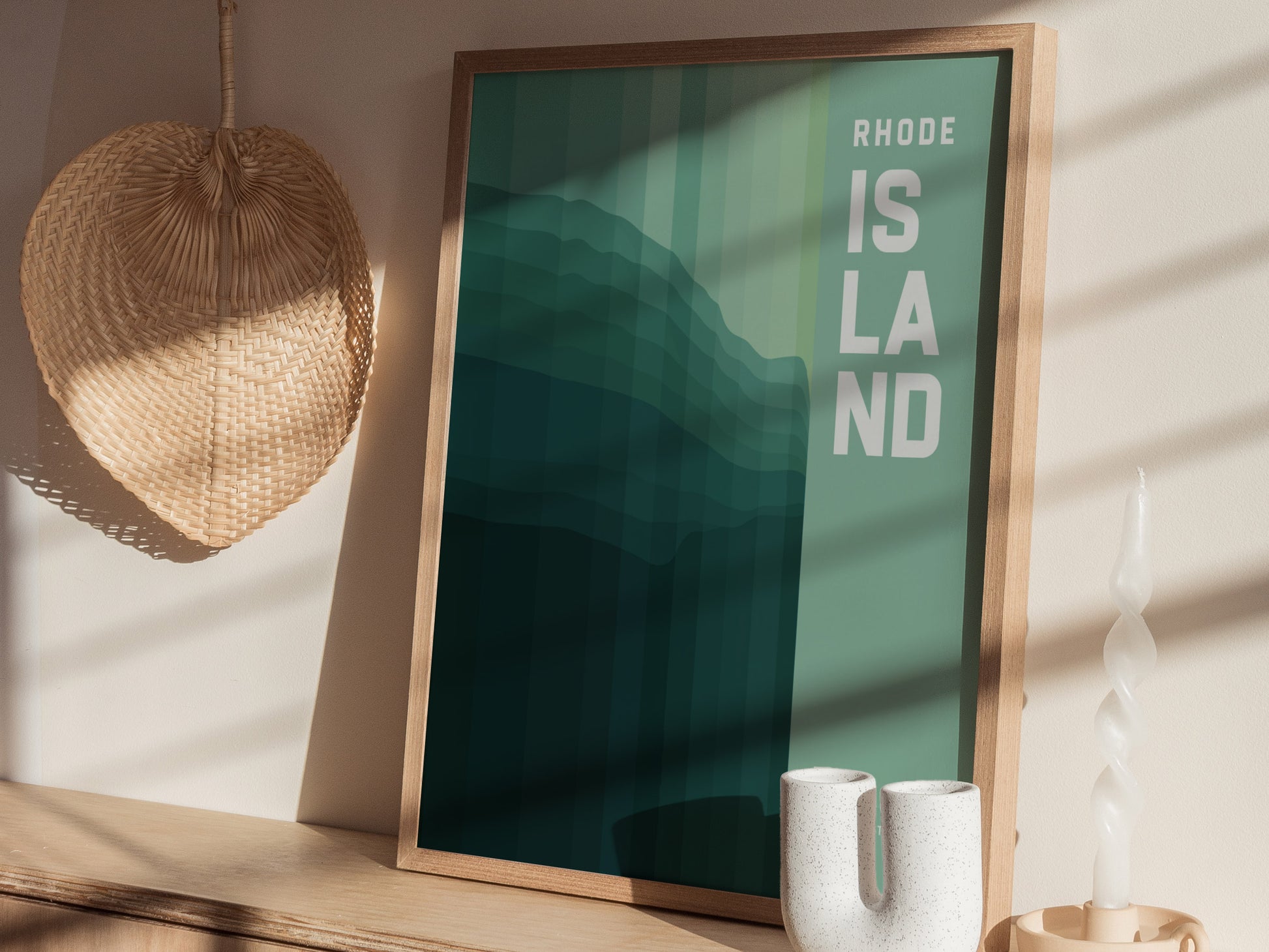 A framed poster with Rhode Island text in bold letters is displayed on a wooden shelf, accompanied by a wicker wall decoration and a white ceramic vase.