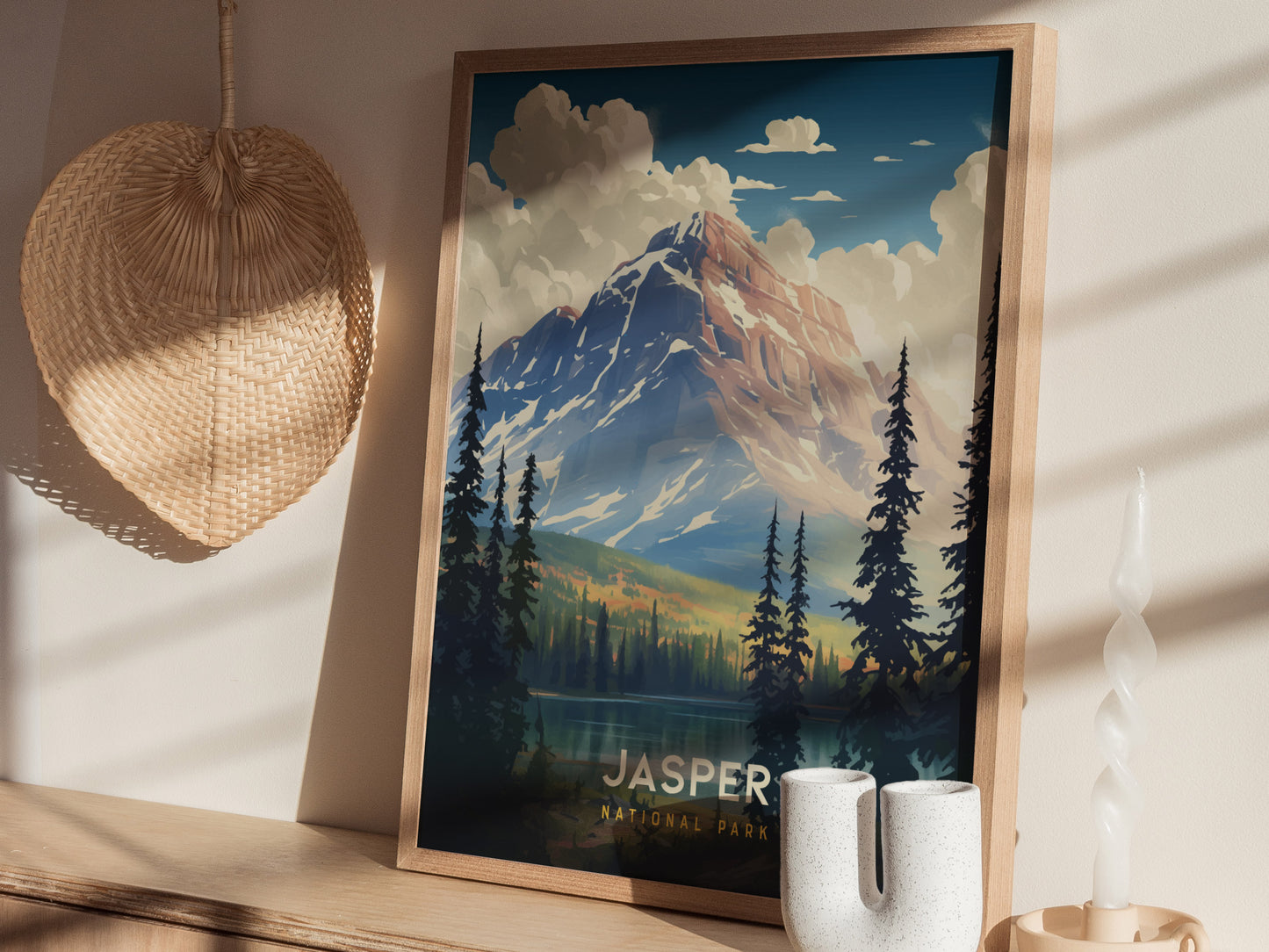 A framed Jasper National Park poster sits on a wooden surface, surrounded by a woven basket and a twisted white candle, showcasing a mountain scene.
