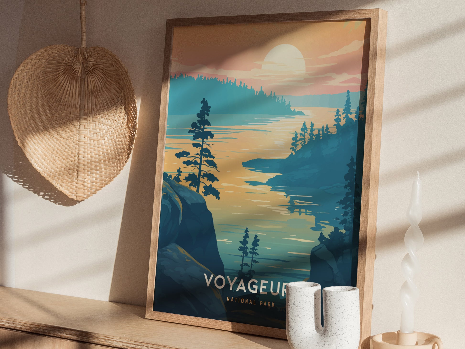 A framed Voyageurs National Park poster rests on a shelf, depicting a serene lake scene at sunset. Nearby, a woven basket hangs on the wall and a twisted candle stands.