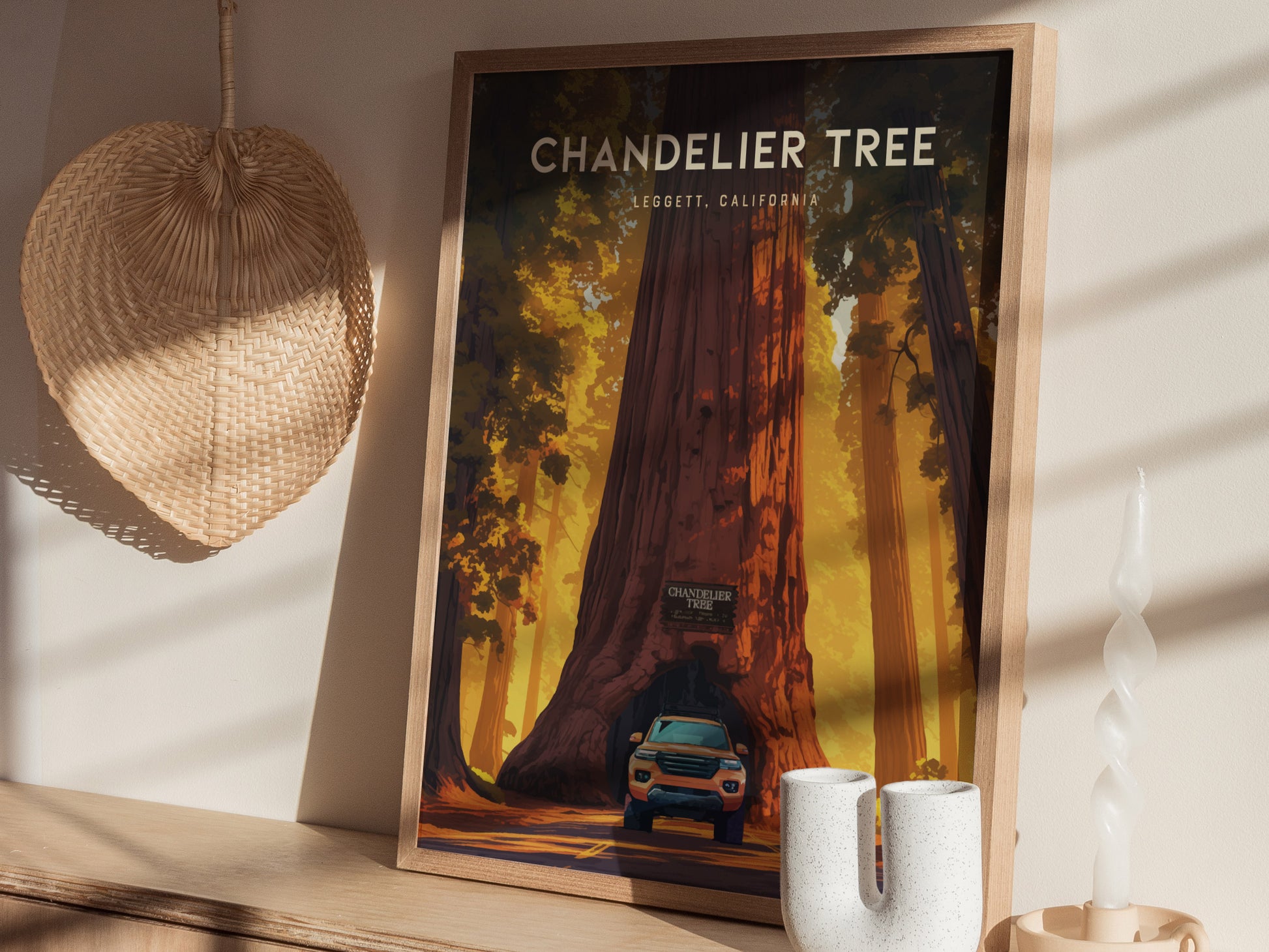 Framed art print depicting the Chandelier Tree with a car driving through its base, displayed on a wooden shelf alongside a woven basket and a spiral candle.
