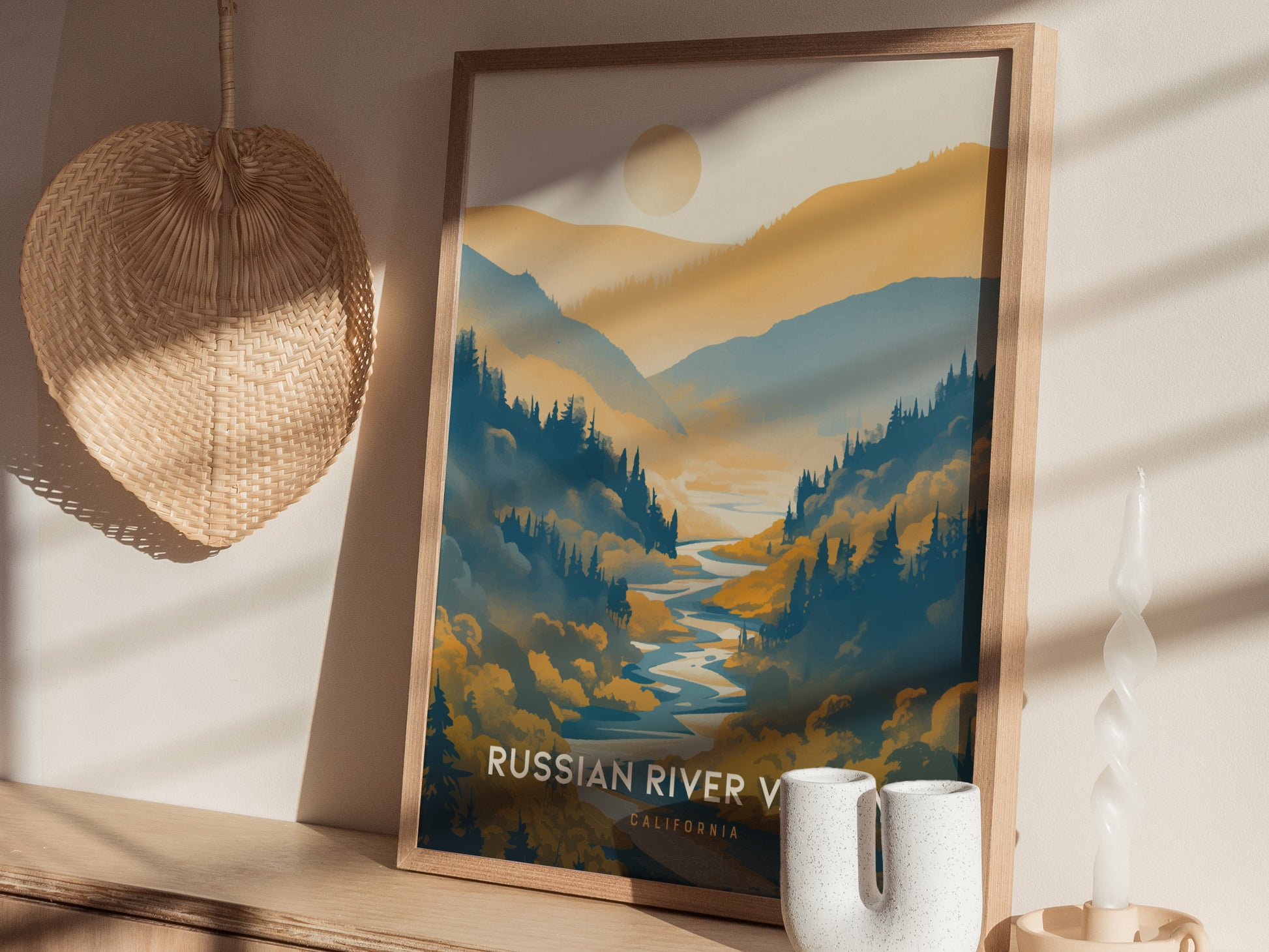 Framed poster of Russian River Valley depicting lush blue and golden hills, with a sun above. It rests on a wooden shelf beside ceramic vases and a woven wall decoration.