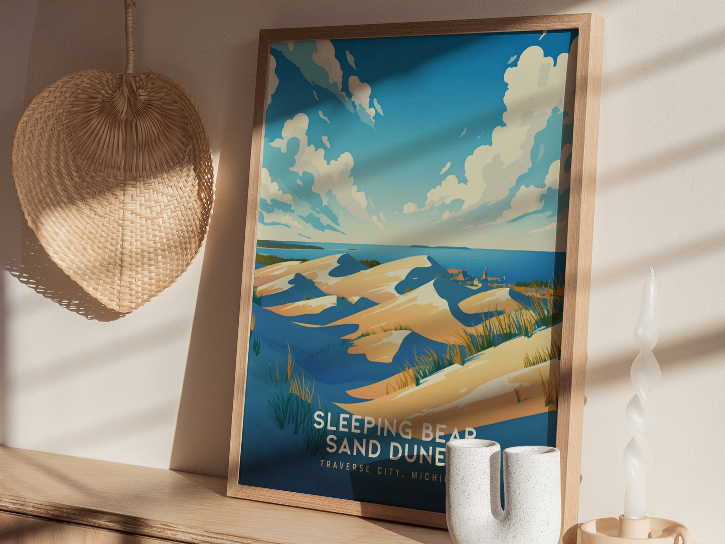 A framed poster of Sleeping Bear Sand Dunes with a vibrant depiction of blue skies and sandy dunes, placed on a wooden shelf beside a woven basket and a unique.