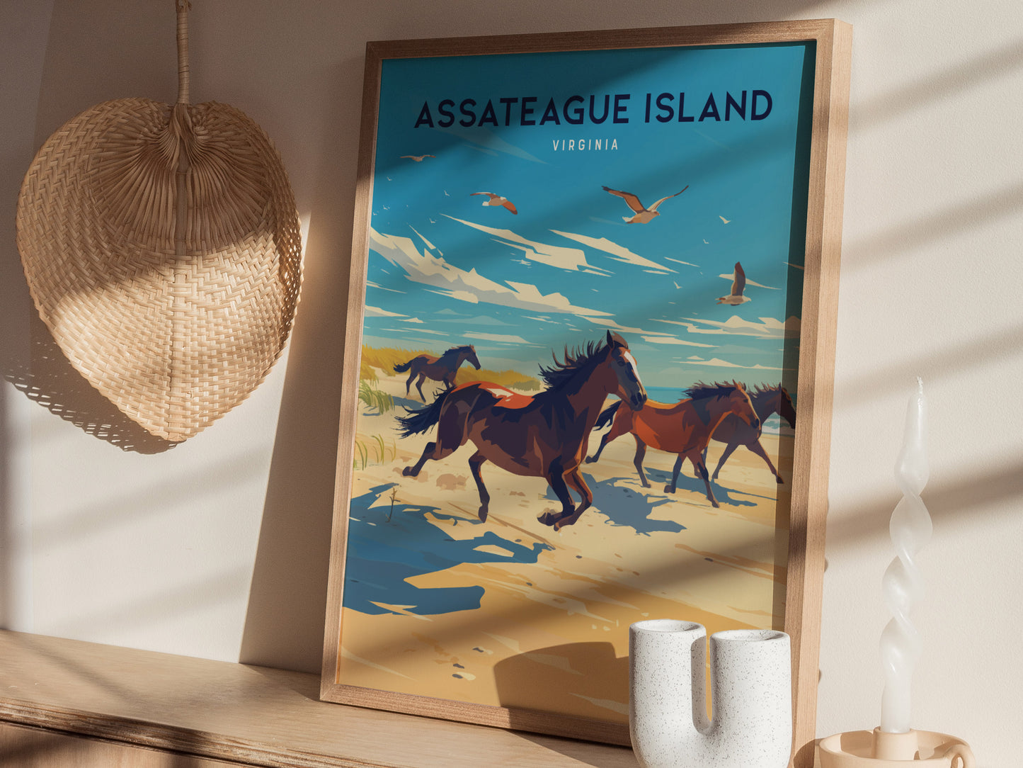 A framed poster of Assateague Island, Virginia, features wild horses running along a beach under a bright blue sky. Its displayed on a wooden shelf with a woven decor piece.