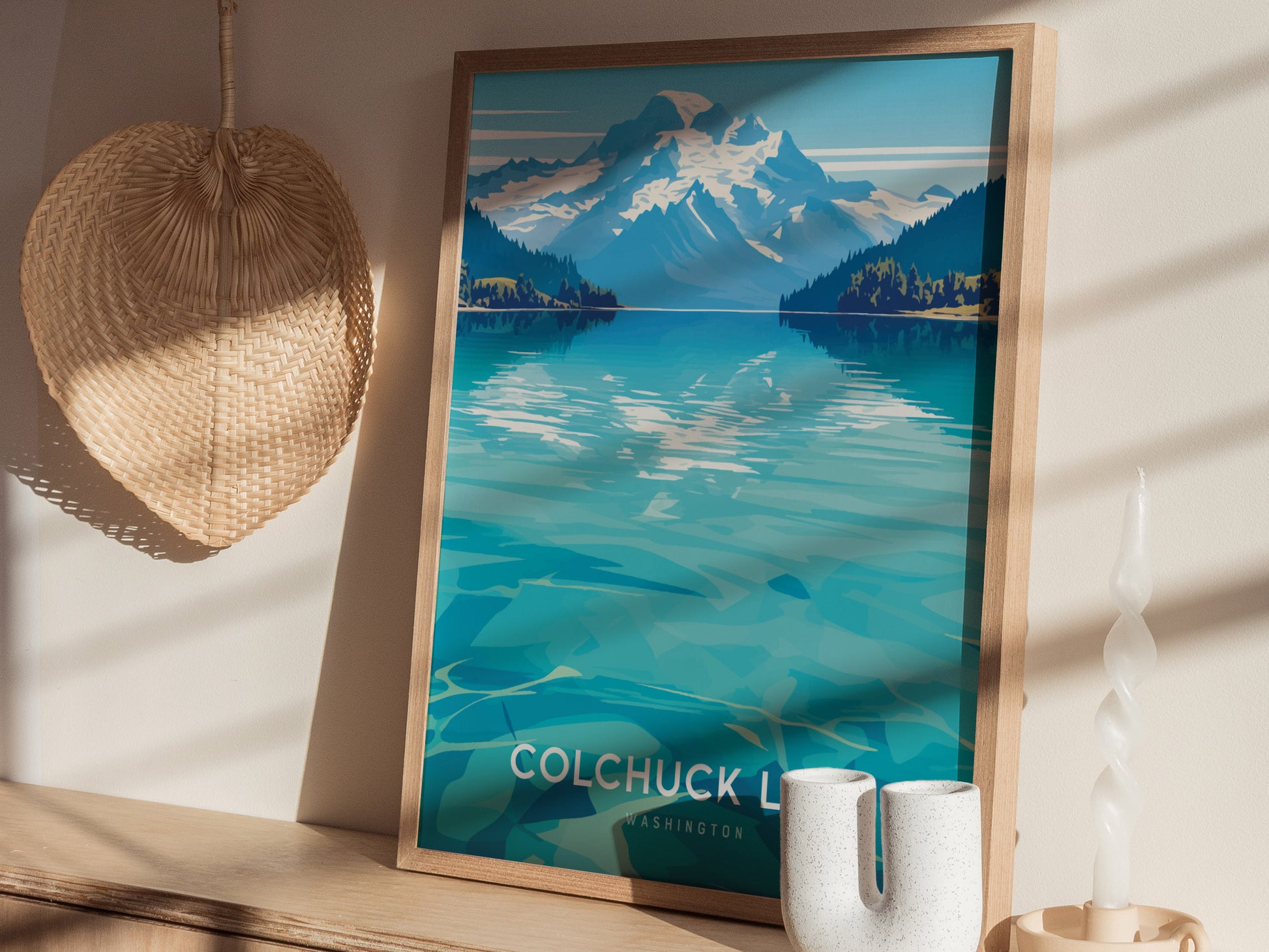 A framed poster of Colchuck Lake with turquoise waters and mountains is displayed on a shelf, accompanied by a woven basket and decorative candle.