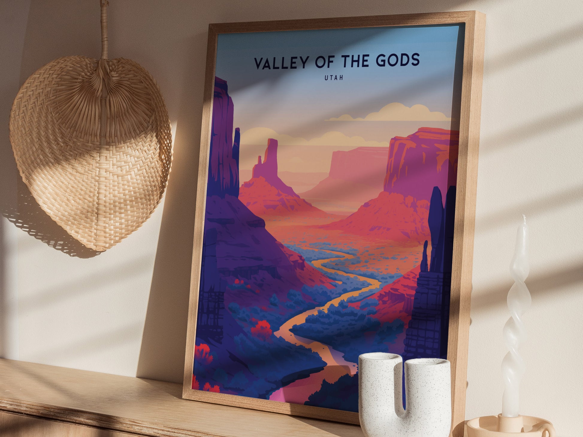 A framed poster titled Valley of the Gods, Utah depicts vibrant red rock formations and a winding river. It rests on a wooden shelf beside a woven basket and decorative.