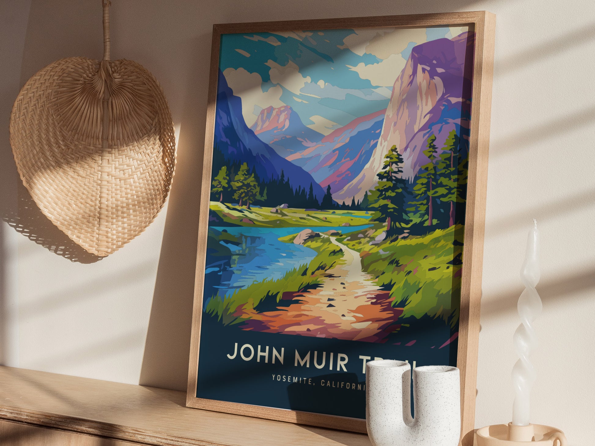 A framed John Muir Trail poster depicting a scenic landscape with mountains, trees, and a river sits on a wooden shelf. Nearby are a woven basket and a twisted candle.