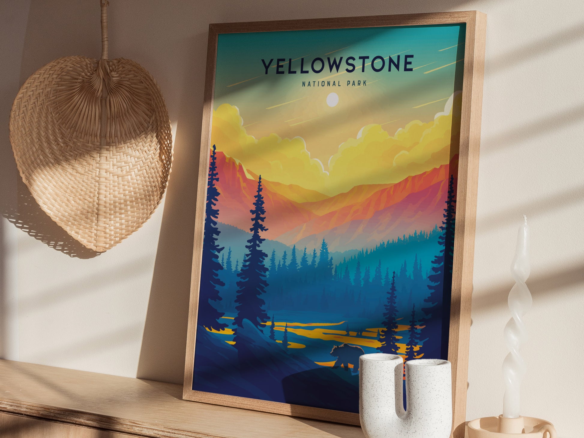 A framed Yellowstone National Park poster featuring a vibrant sunset, silhouetted trees, and a bear, displayed on a wooden surface with a woven basket and unique candle nearby.
