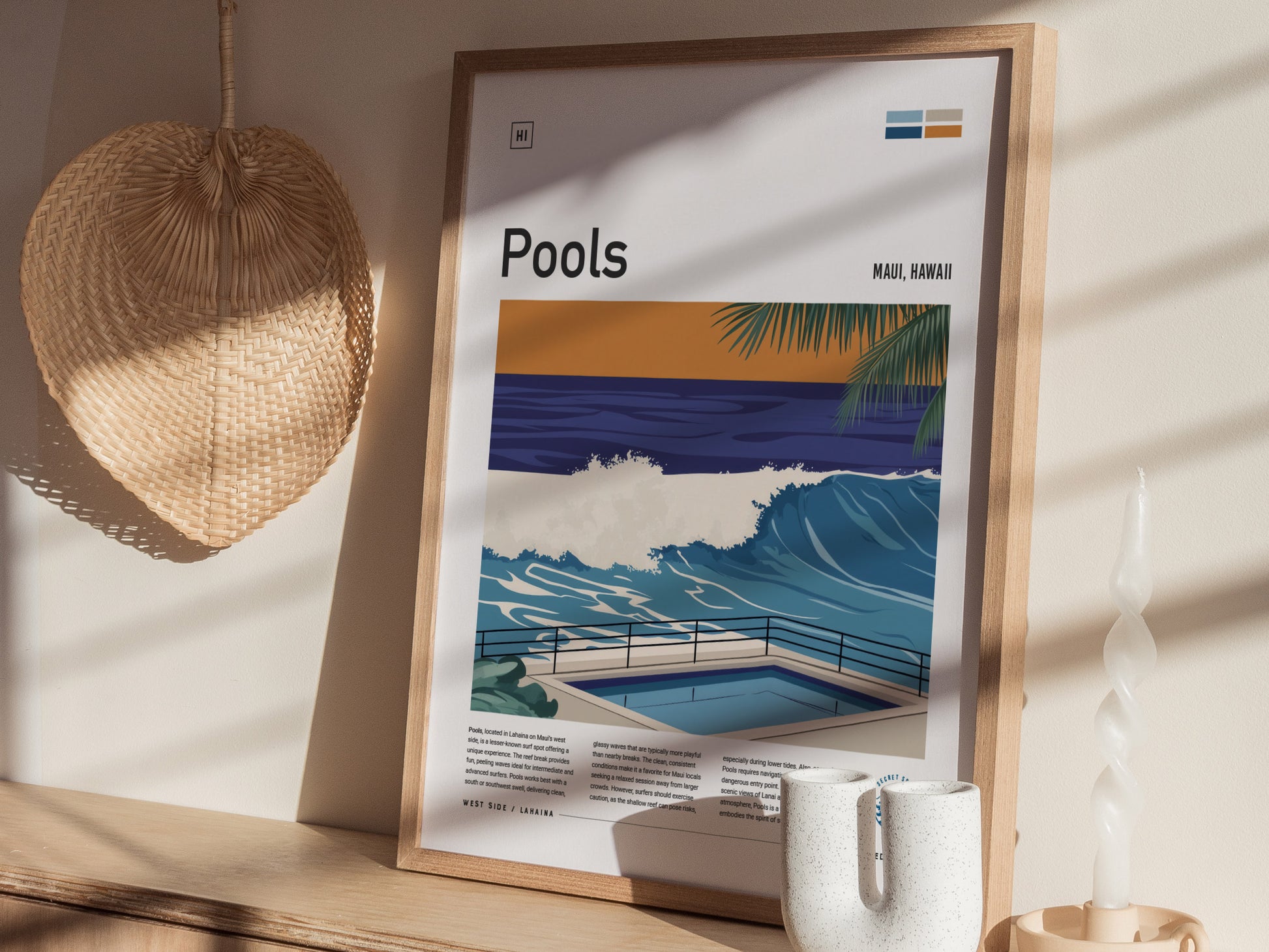 A framed poster titled Pools depicting a vibrant ocean wave scene in Maui, Hawaii, sits on a shelf beside a woven hat and a twisted candle.