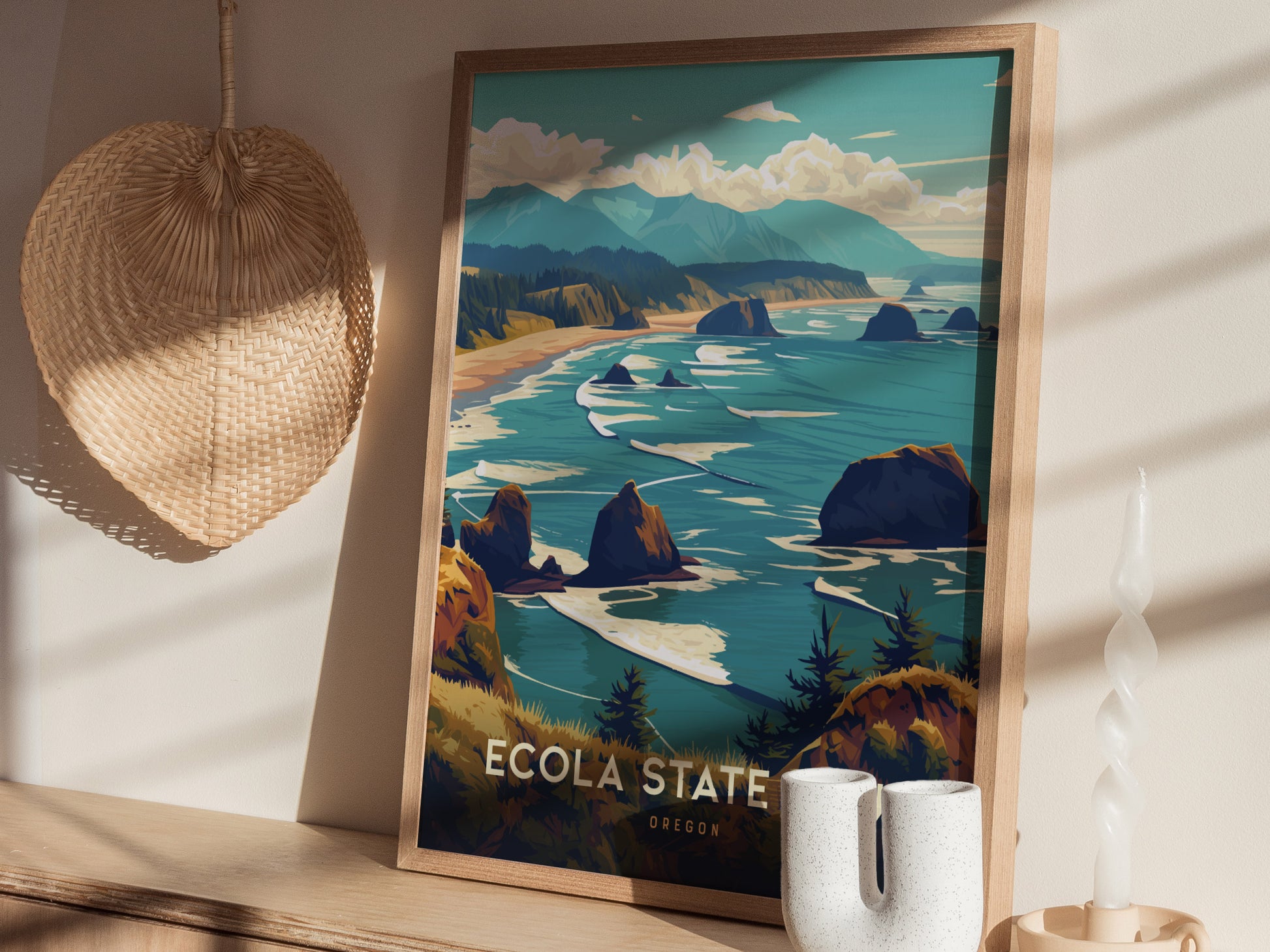 Framed Ecola State Park poster depicting a vibrant coastal landscape with cliffs and ocean, resting on a wooden surface alongside a woven basket and decorative candles.