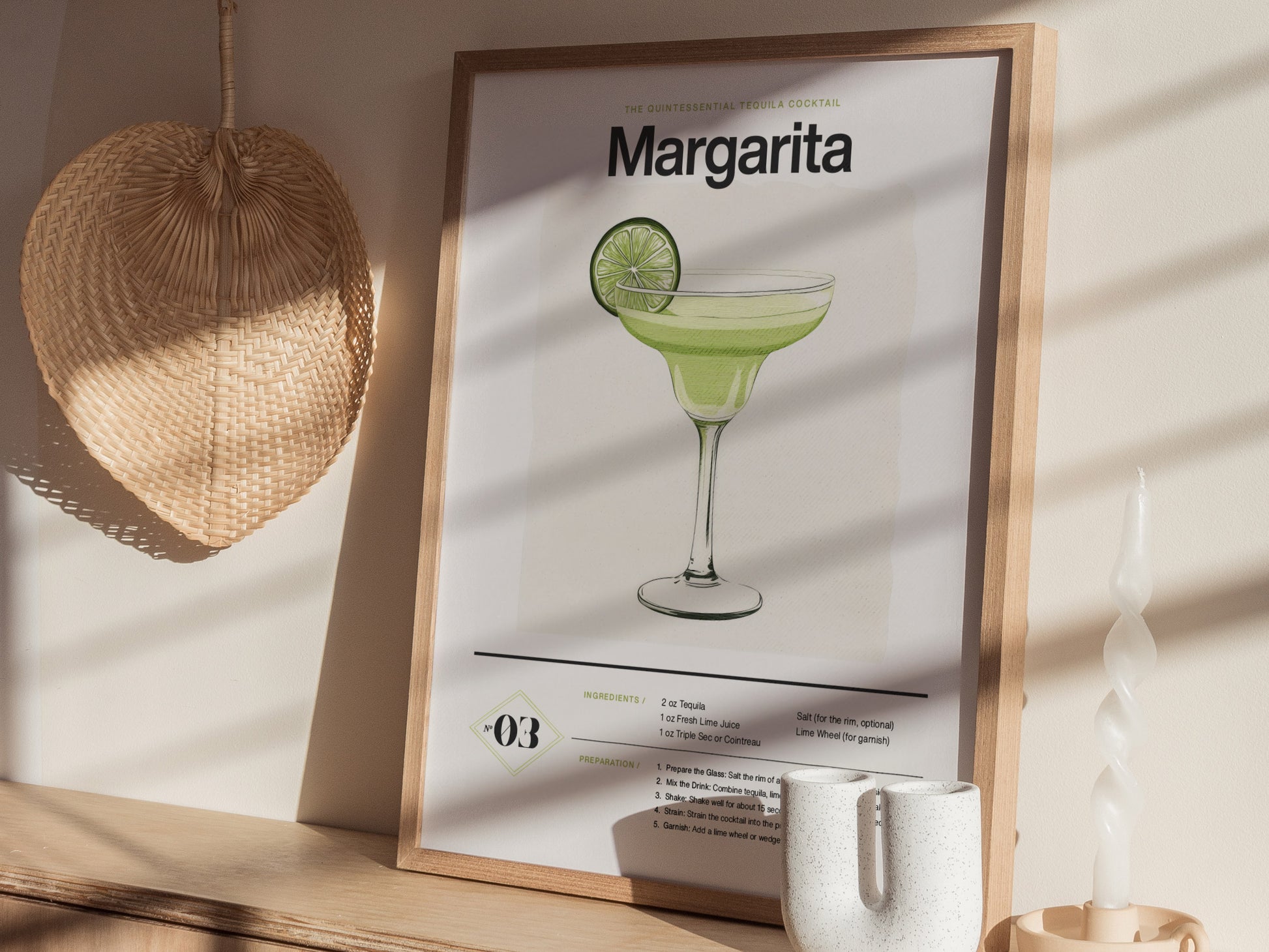 A framed Margarita cocktail poster with an illustrated drink and lime slice sits on a wooden shelf. Nearby, a woven fan and twisted candle add decorative elements.