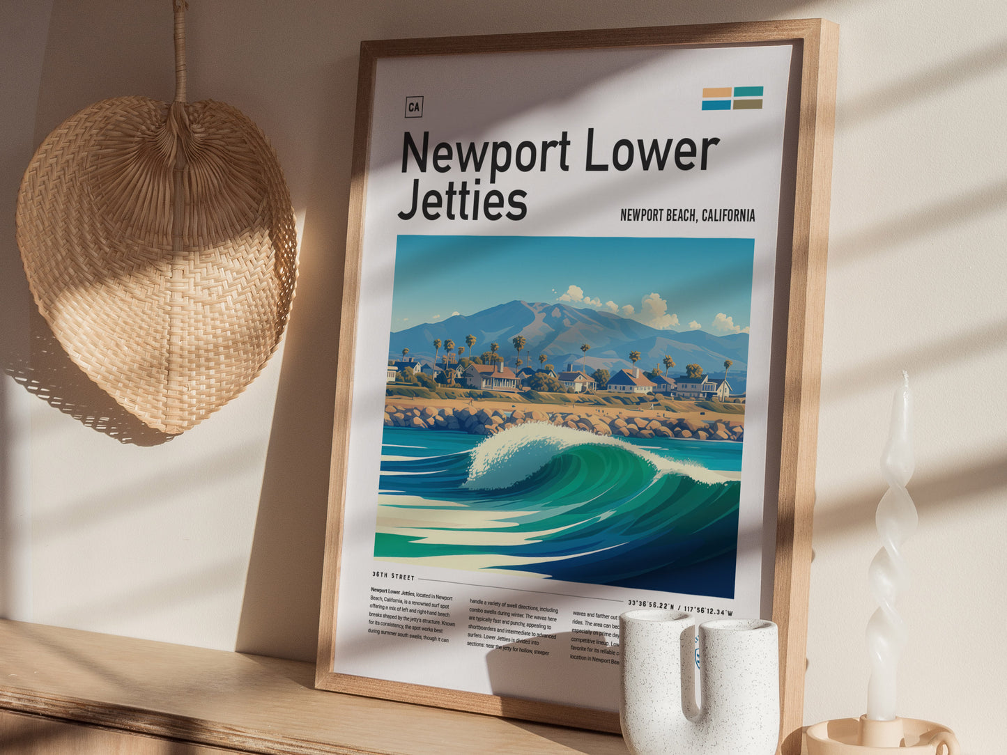 A framed Newport Lower Jetties poster featuring a coastal scene with waves and mountains is displayed on a wooden shelf alongside a woven basket and a twisted candle.