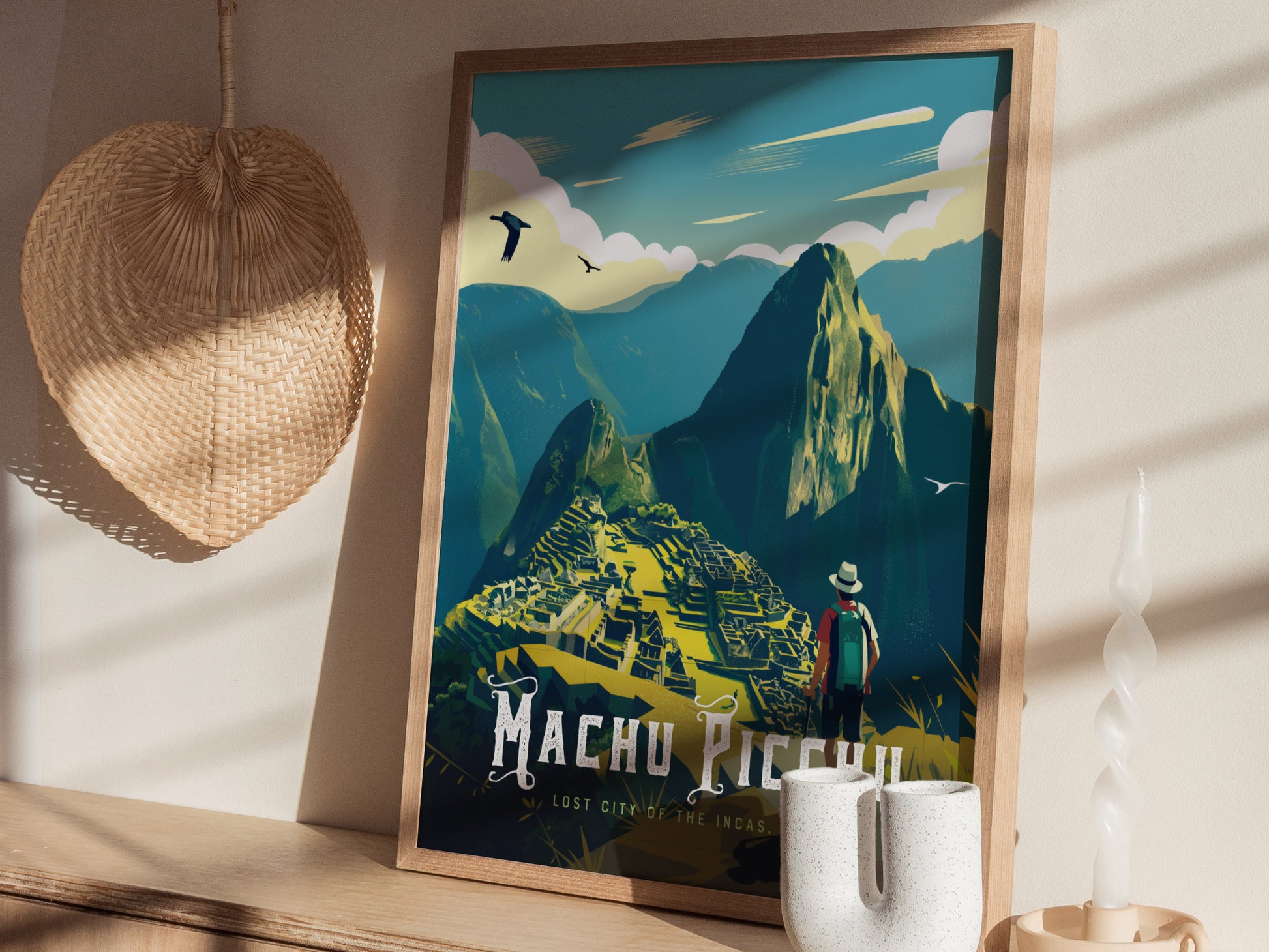 A framed poster of Machu Picchu, featuring a hiker overlooking the ancient ruins and mountains, is displayed on a wooden shelf alongside a woven hat and decorative candle.