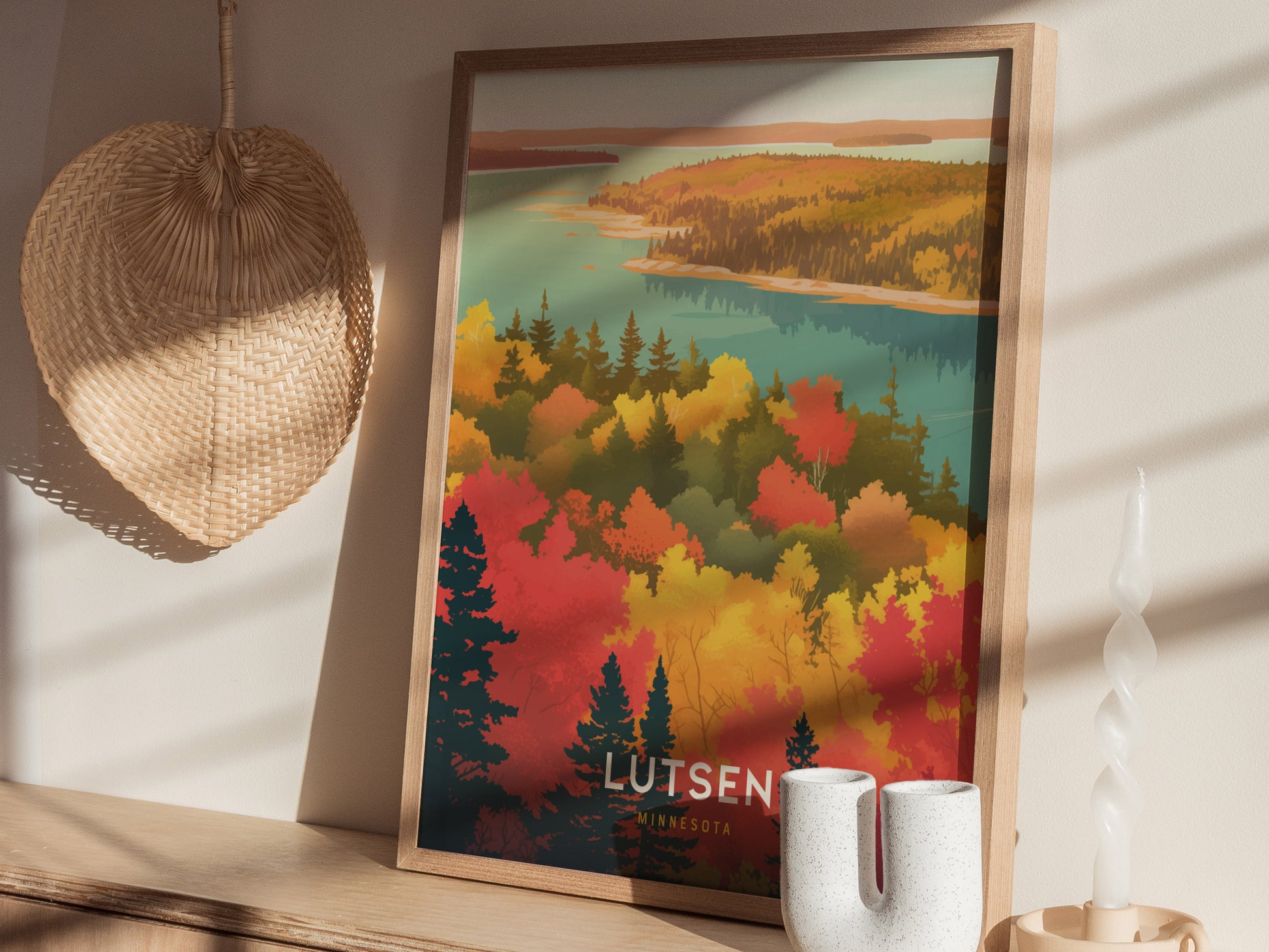 A framed poster depicting colorful autumn foliage in Lutsen, Minnesota, rests on a wooden shelf. Nearby, a woven wall decoration and a twisted candle create a cozy atmosphere.