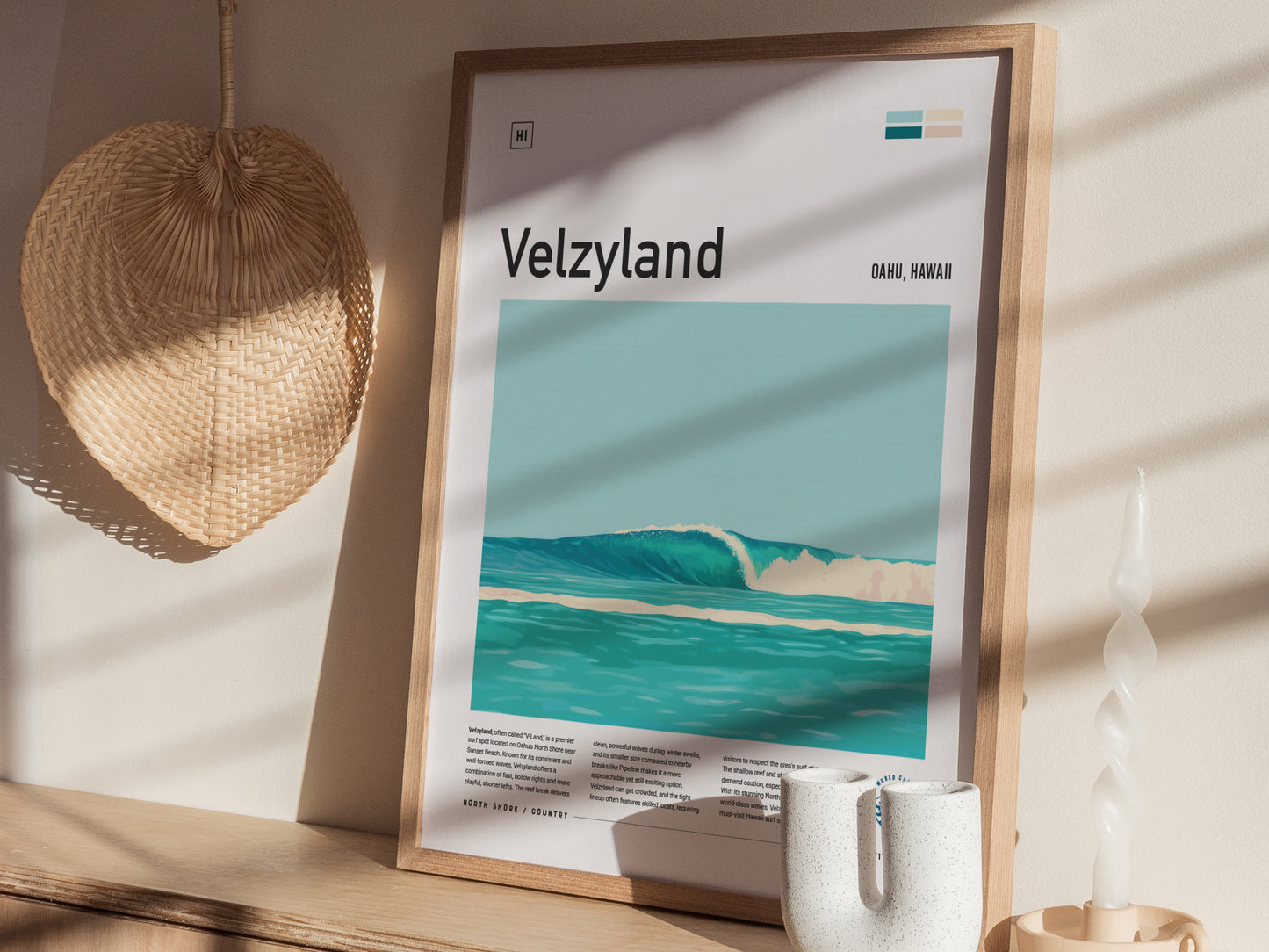 A framed poster titled Velzyland depicting turquoise waves is displayed on a wooden surface, with a woven fan and a spiral candle nearby, creating a serene coastal vibe.