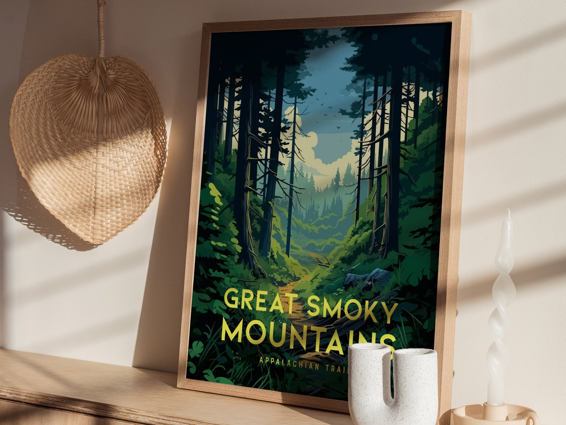 A framed poster of the Great Smoky Mountains, featuring a lush forest scene, is displayed on a wooden shelf next to a woven decorative item and a twisted candle.