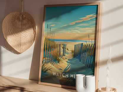 A framed poster depicting a sandy beach with a wooden fence leading to the ocean under a colorful sky. It sits on a shelf next to a woven hat and.