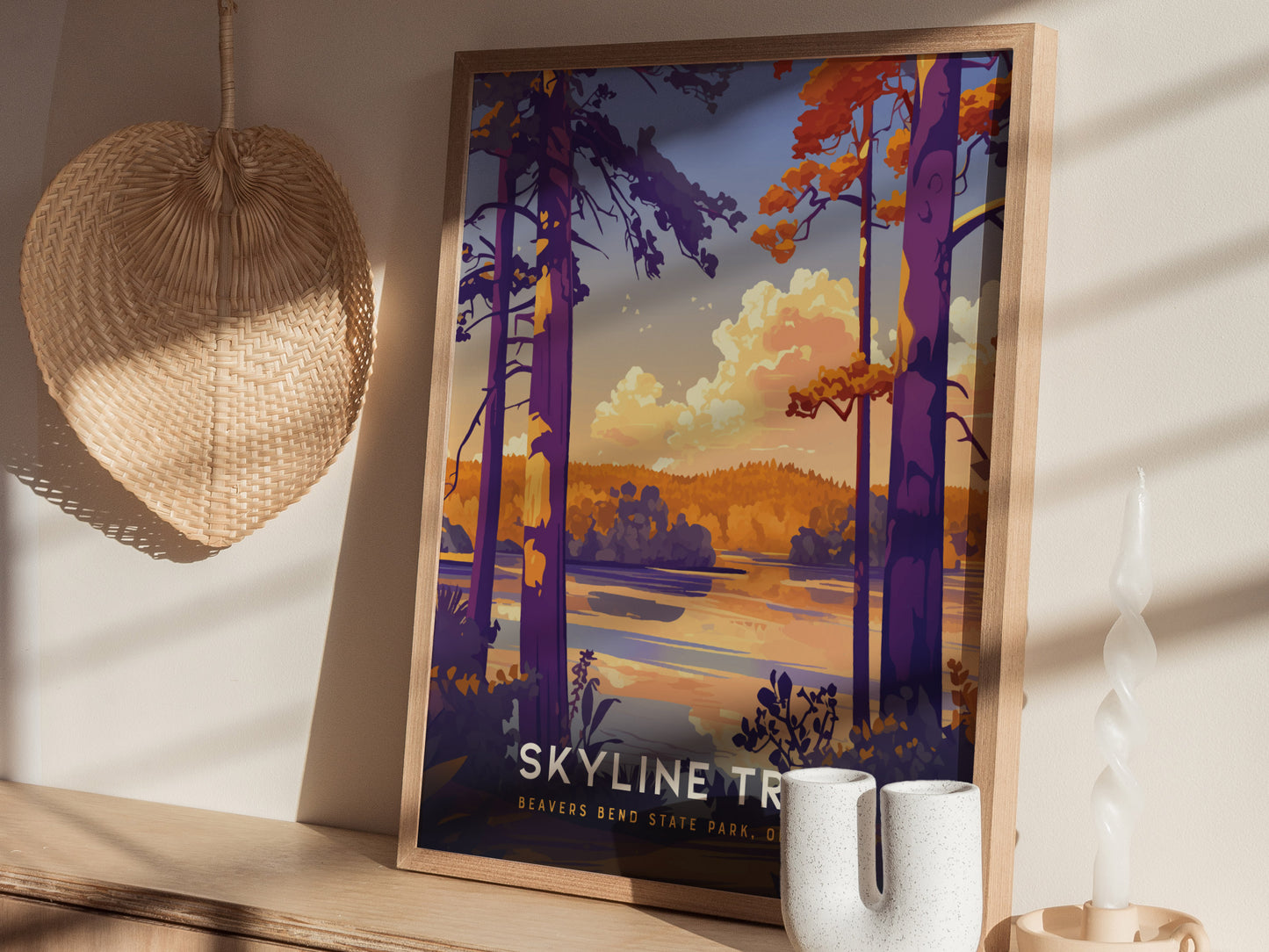 A framed poster of Beavers Bend State Parks Skyline Trail leaning against a wall, surrounded by warm decor including a woven fan and ceramic vases.