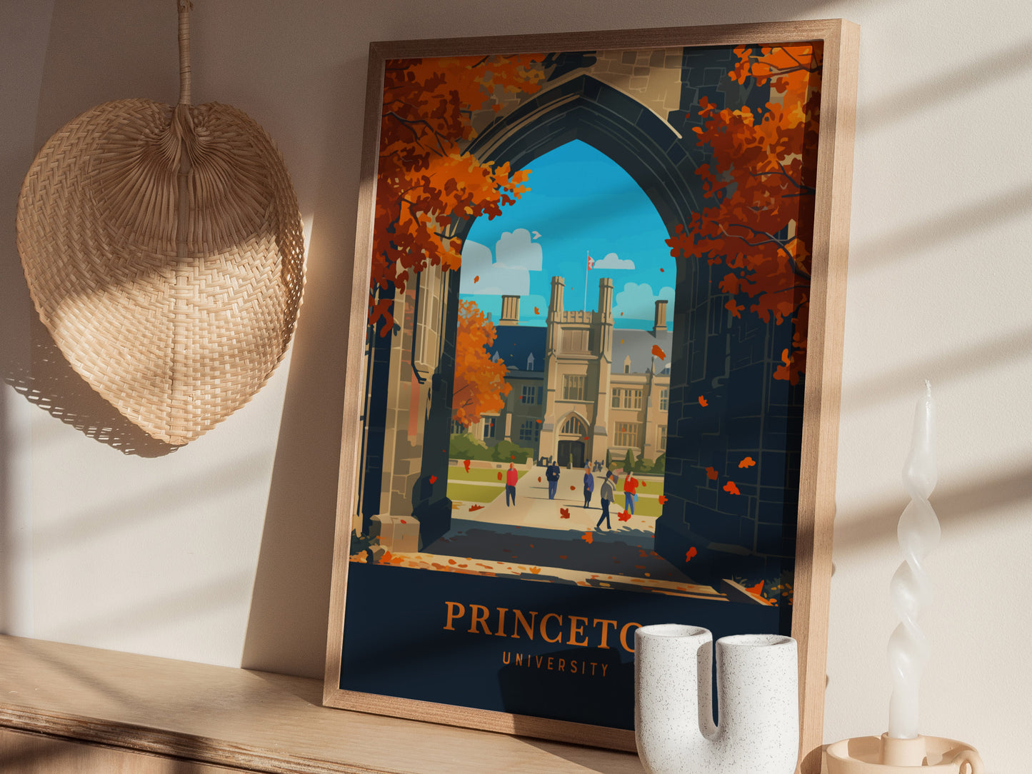 A framed Princeton University poster featuring Gothic architecture and autumn foliage sits on a wooden shelf, alongside a woven basket and a unique ceramic vase.