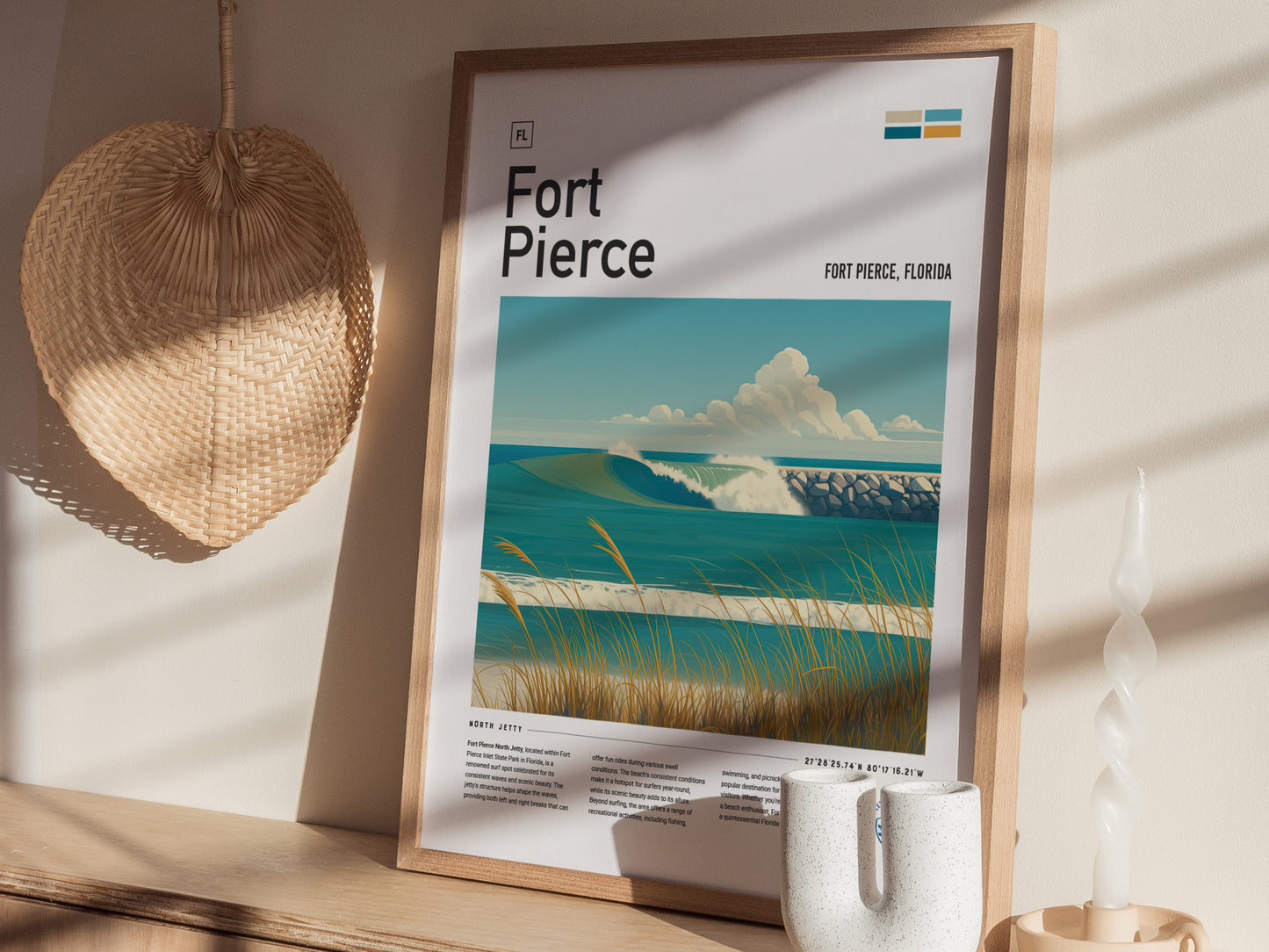 A framed poster of Fort Pierce, Florida, featuring ocean waves and a jetty, is displayed on a wooden shelf beside a woven fan and a twisted white candle.