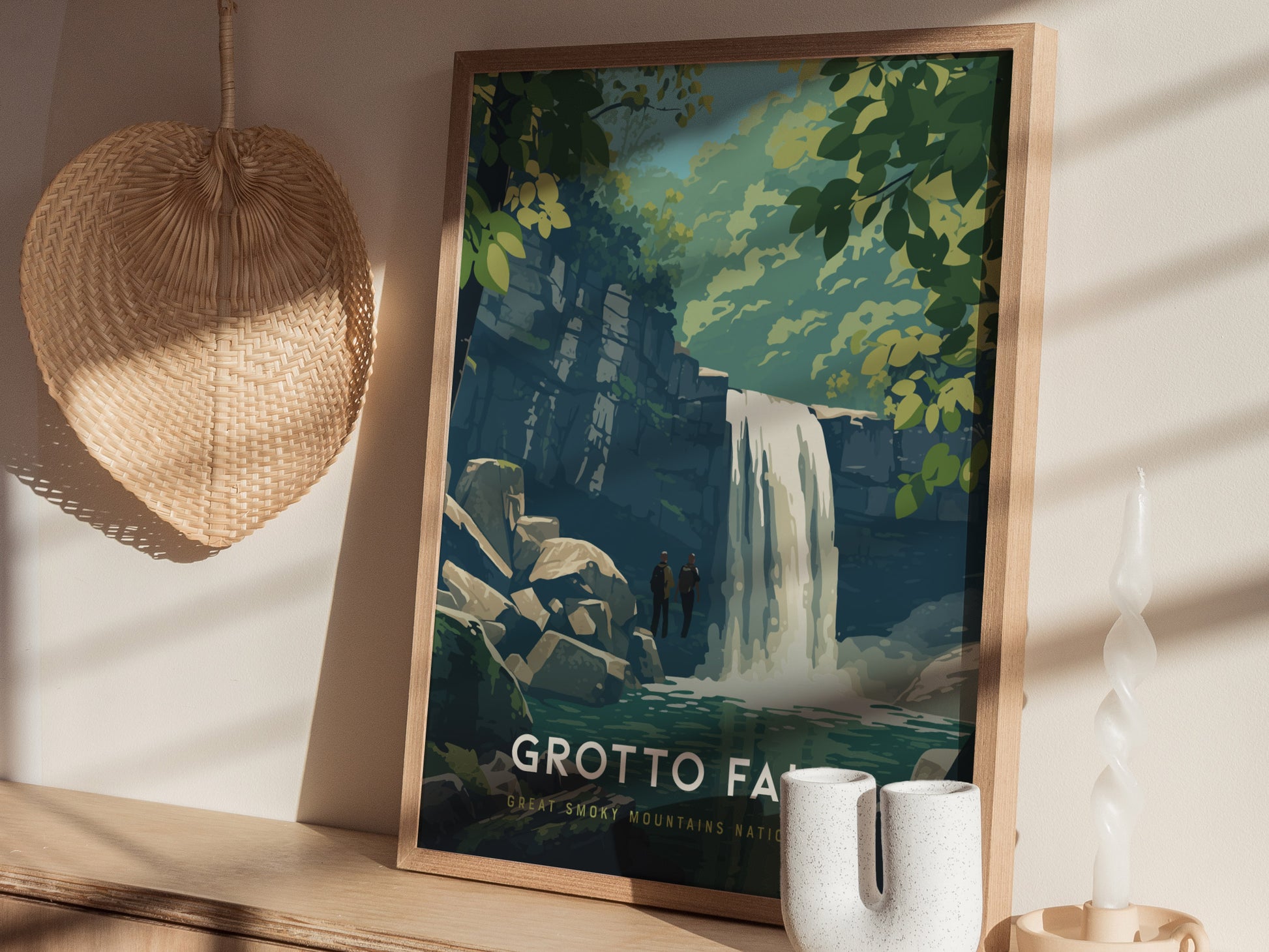 A framed poster of Grotto Falls is displayed on a shelf, depicting a serene waterfall surrounded by lush greenery. The setting includes a wicker wall decoration and a twisted candle, creating a cozy atmosphere.
