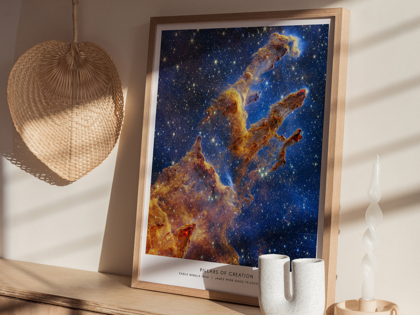 Framed Pillars of Creation JWST print resting on a wooden surface, displayed at an angle to show the celestial colors and detailed nebula structure.