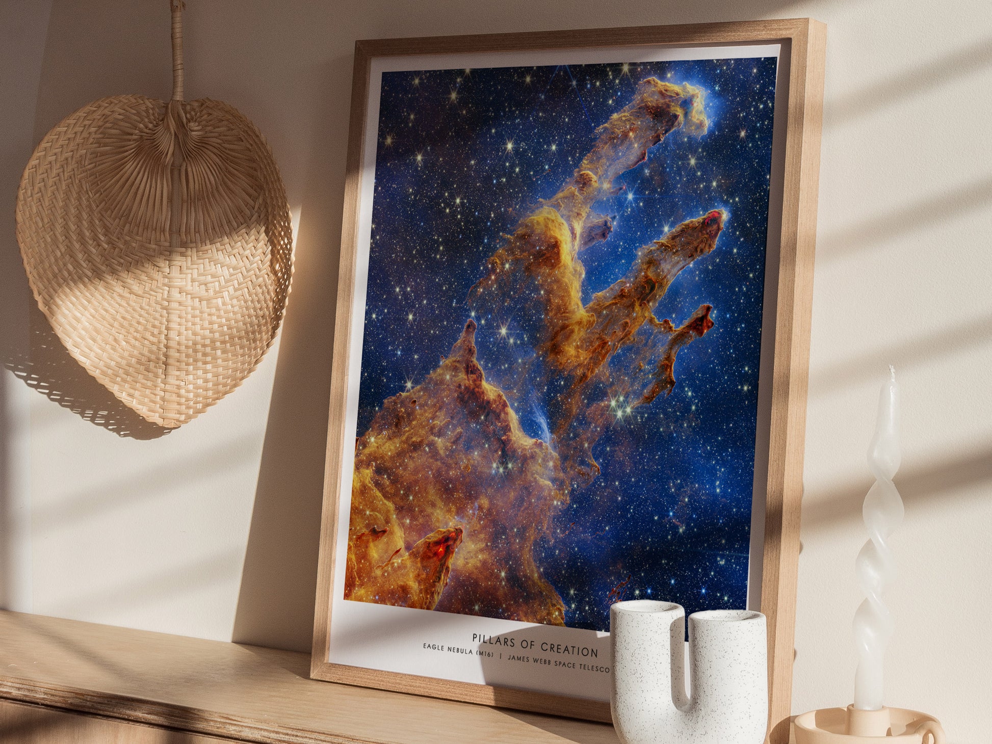 Framed Pillars of Creation JWST print resting on a wooden surface, displayed at an angle to show the celestial colors and detailed nebula structure.