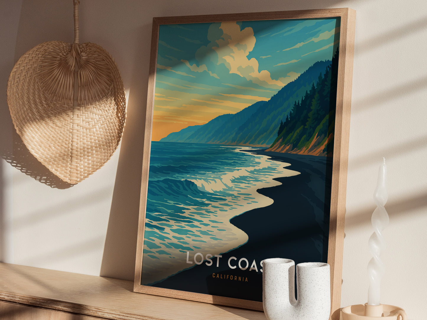 A framed poster titled Lost Coast California features a serene coastal scene with gentle waves lapping at a dark beach, surrounded by lush green hills under a colorful sunset sky. The artwork evokes a peaceful, natural atmosphere.