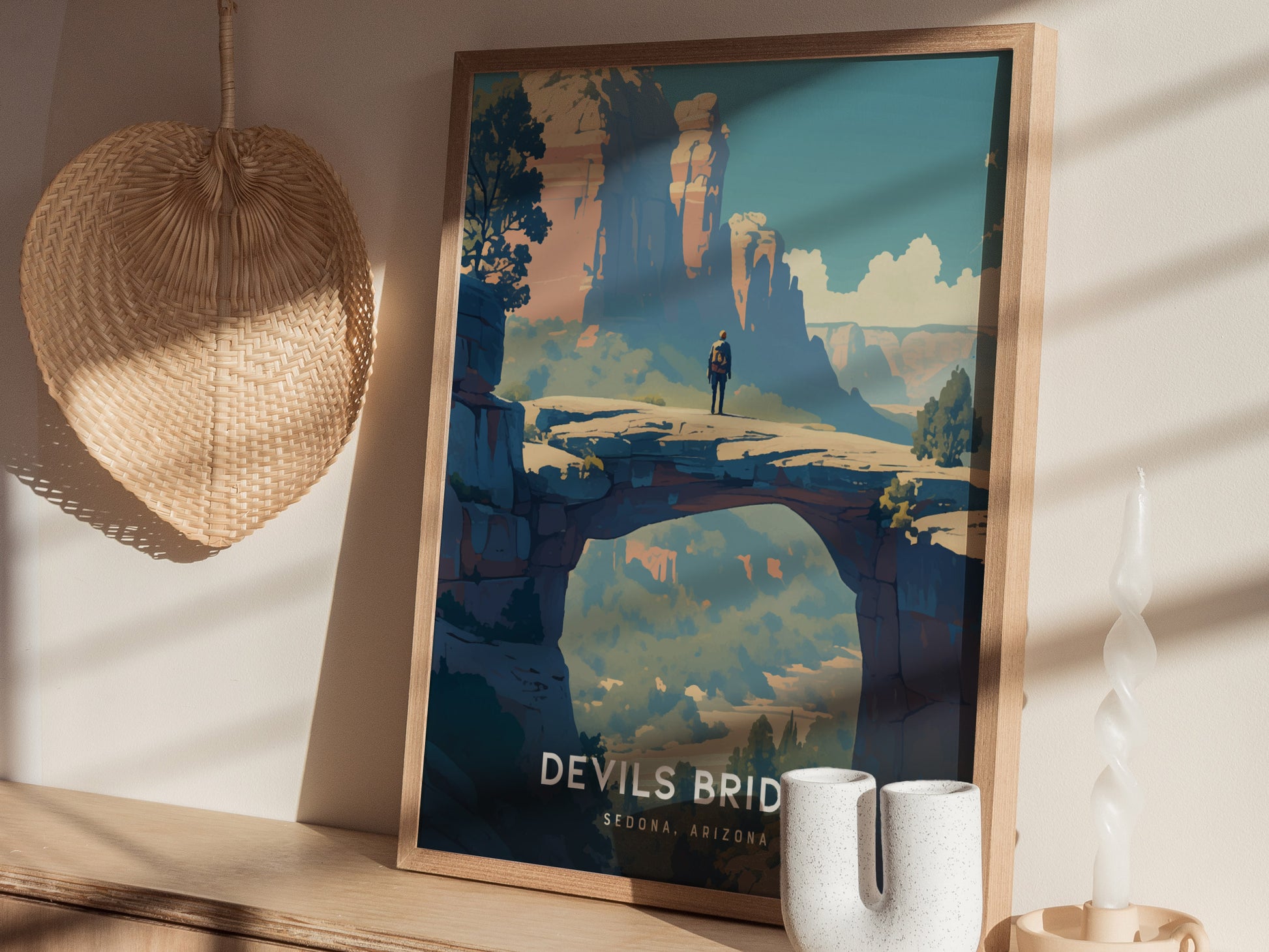 A framed poster of Devils Bridge in Sedona, Arizona, featuring a person standing on a natural sandstone arch against a backdrop of cliffs, displayed on a wooden shelf.