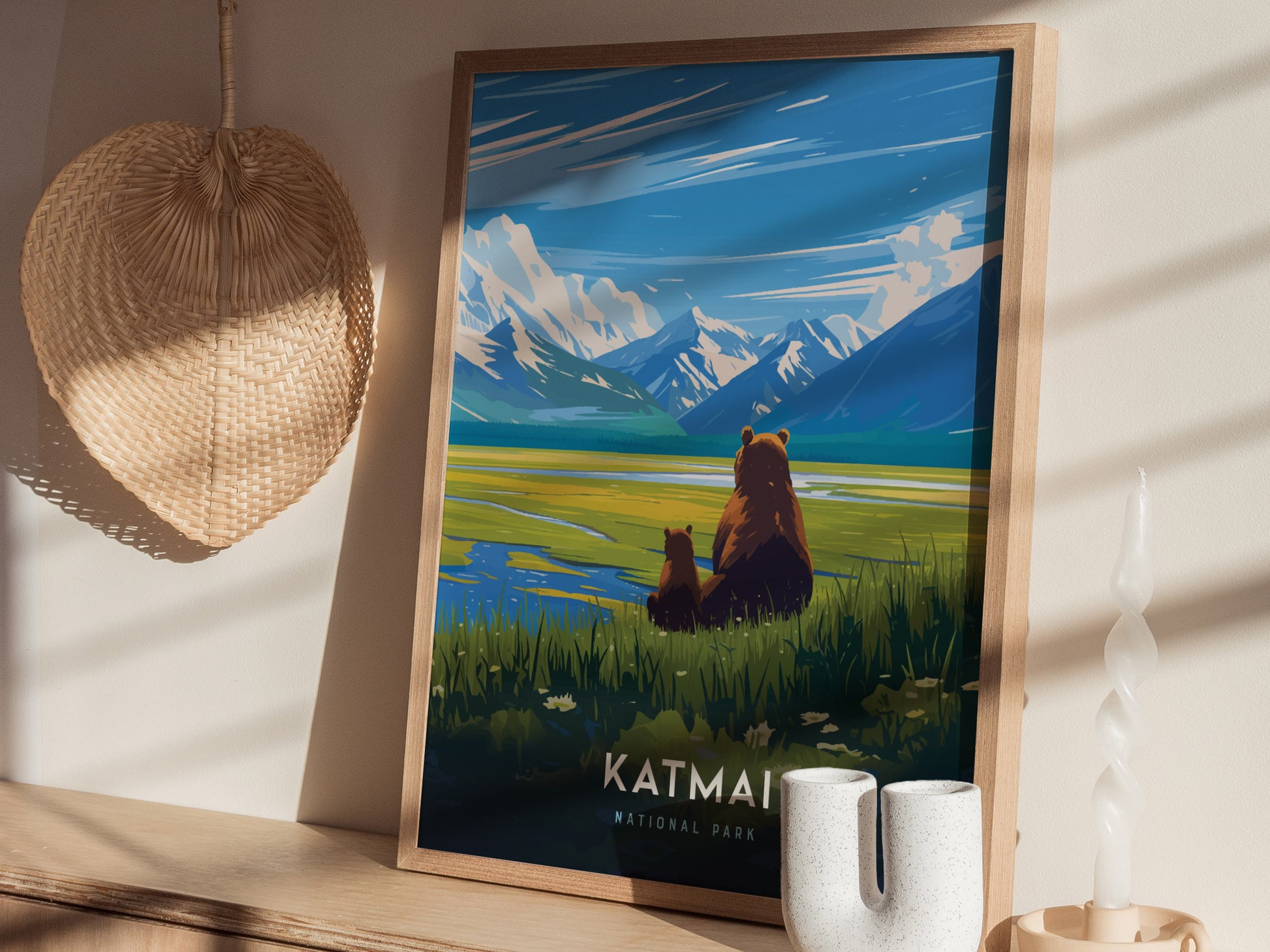 A framed poster of Katmai National Park featuring a bear and cub overlooking a lake with mountains in the background, displayed on a wooden shelf with a woven basket and.