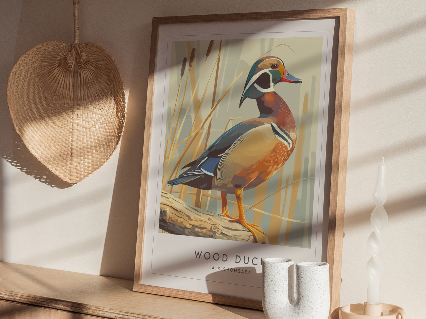 A framed artwork of a wood duck stands on a light-colored surface, surrounded by natural decor. The illustration features the vibrant bird perched on a log with tall grasses in the background, showcasing warm colors and a contemporary.