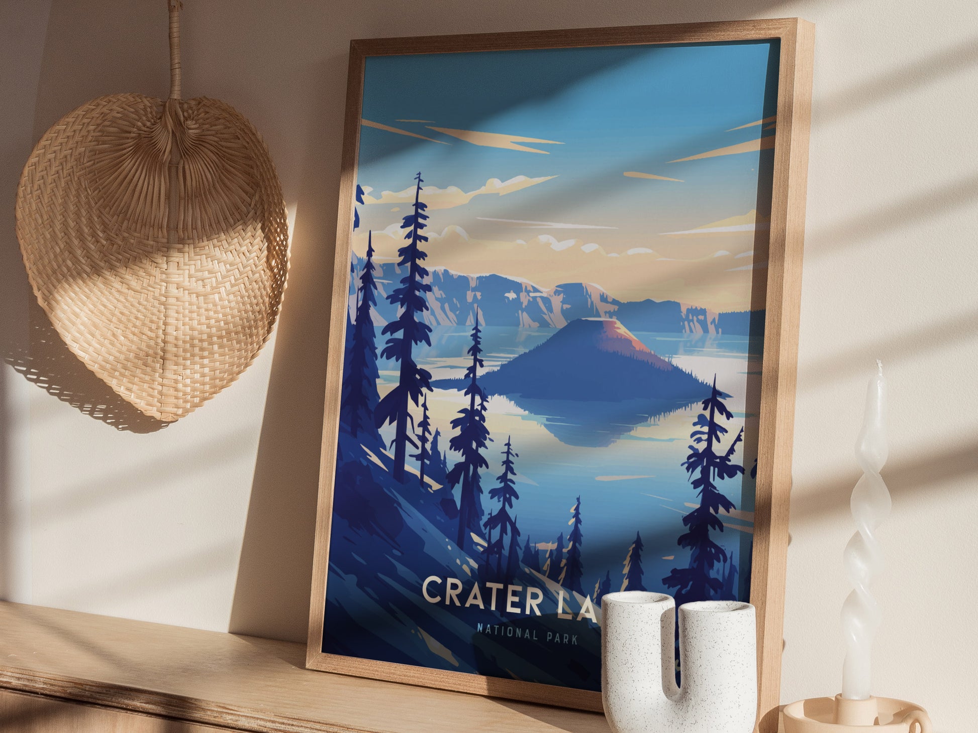A framed poster of Crater Lake National Park features vibrant blues and a serene landscape, displayed on a wooden shelf next to a wicker basket and a white candle.
