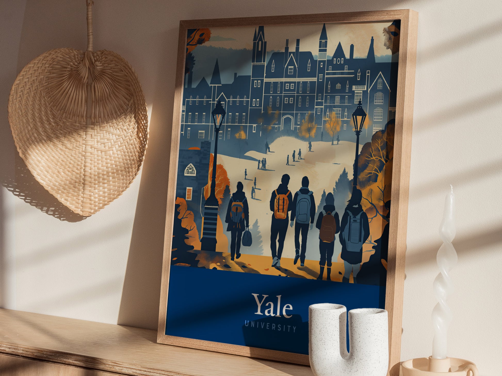 A framed poster of Yale University features a stylized illustration of people walking towards Gothic architecture. Its placed on a wooden shelf next to a woven fan and ceramic vases.
